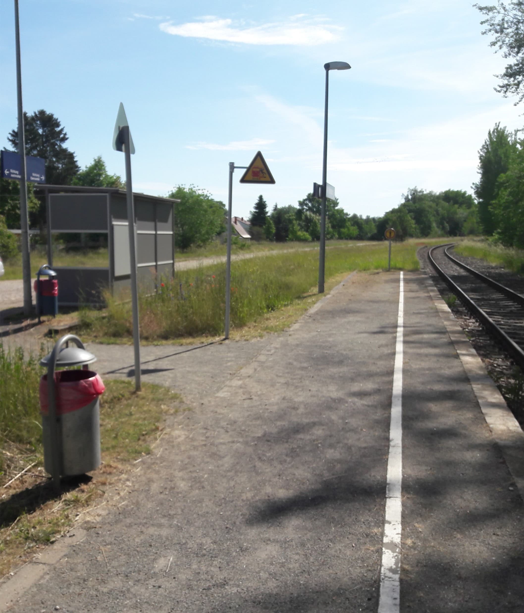 Ein Bahnsteig, mit Mülleimern und einem Wetterschutzhäuschen.