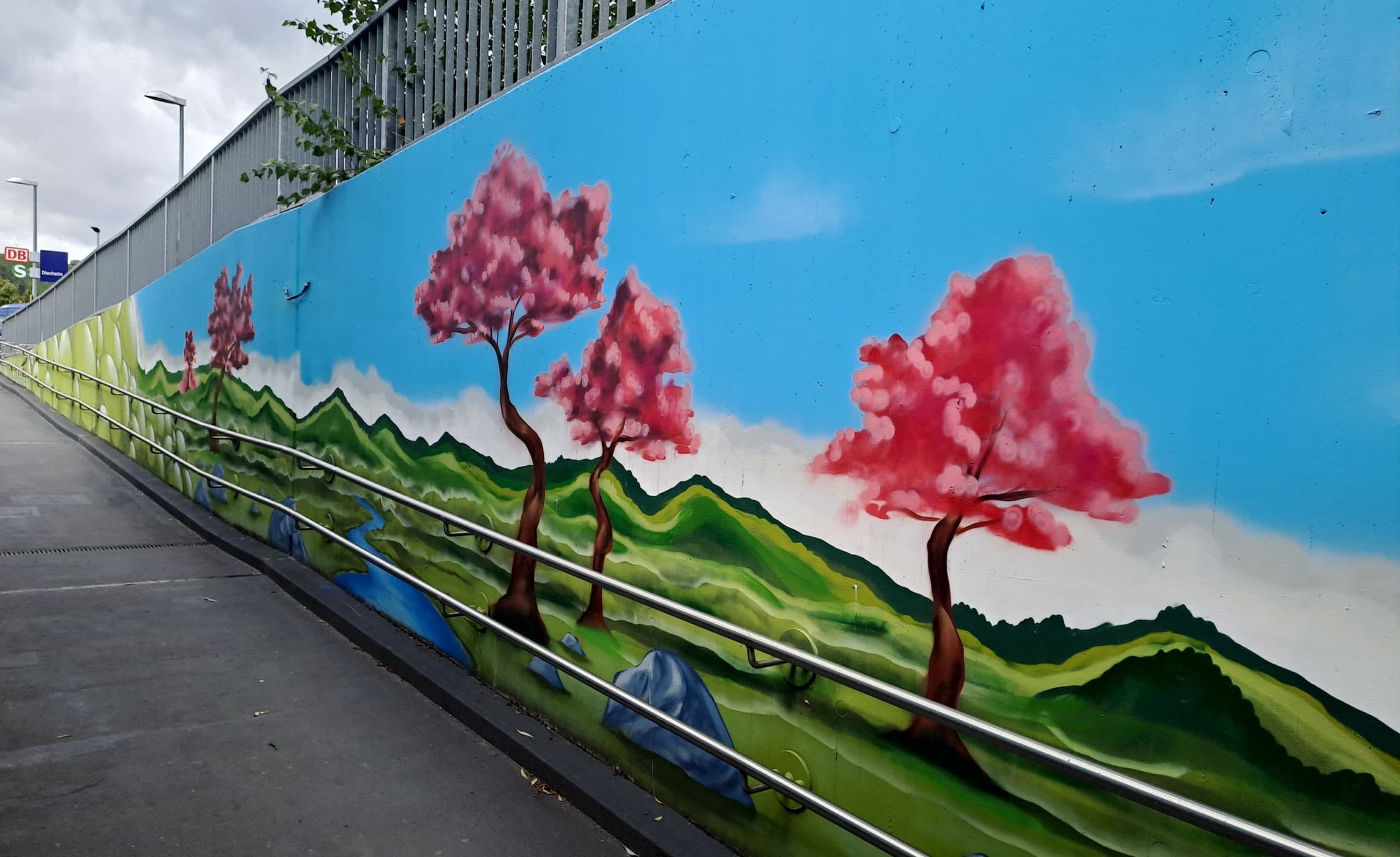 Hügelige, grüne Landschaft mit rot-rosa-blühenden Bäumen auf eine Wand der Rampe gemalt.