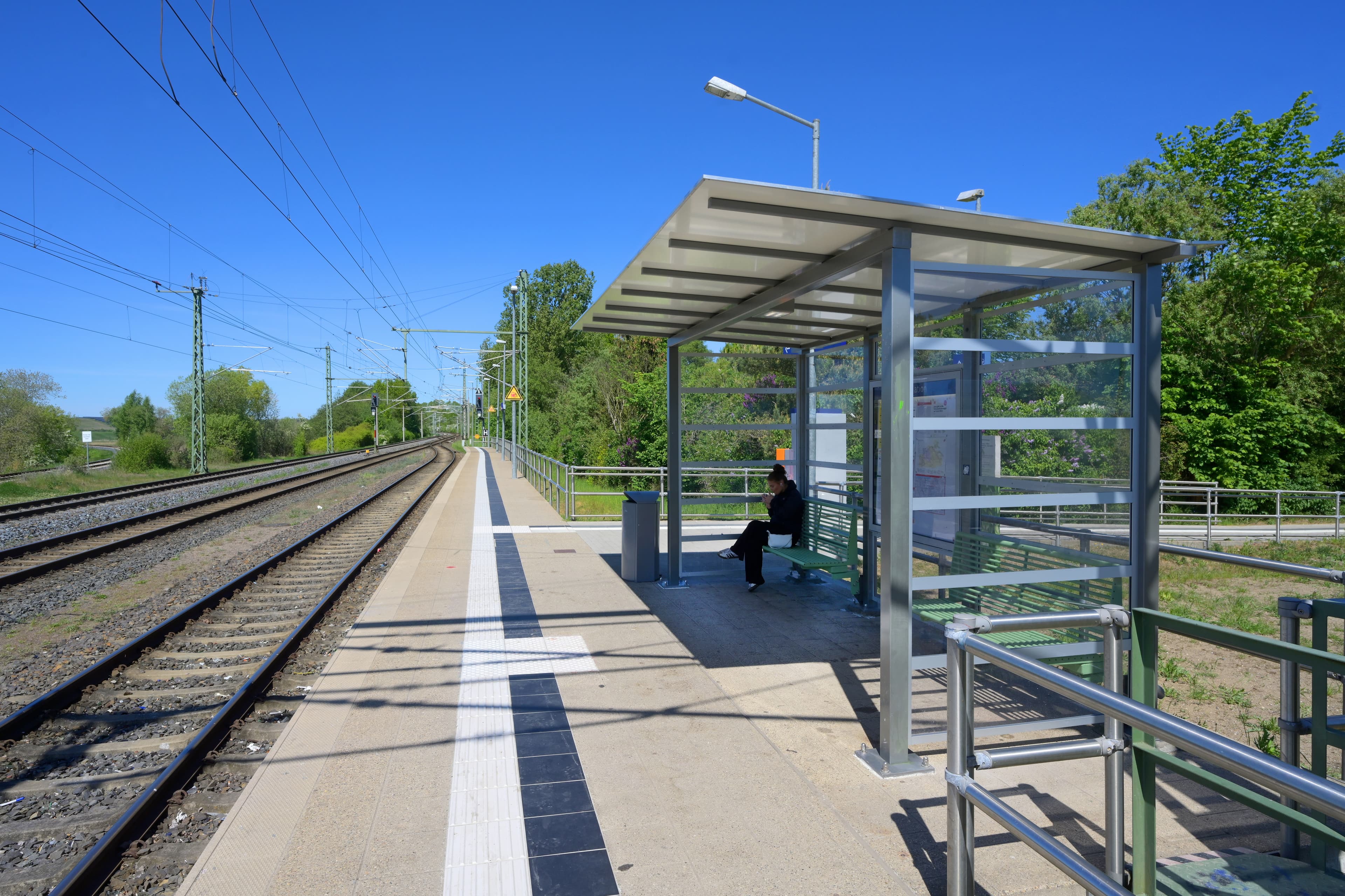 Ein Bahnsteig mit transparentem Wetterschutzhäuschen.