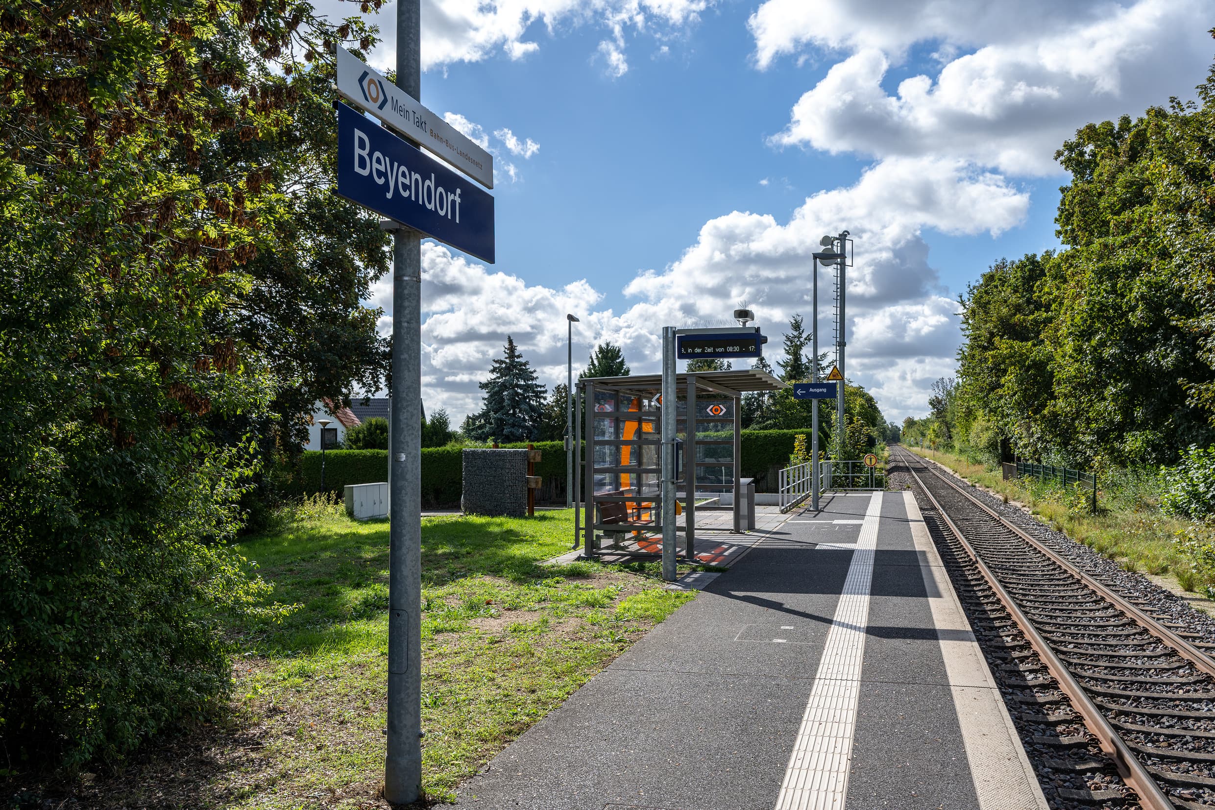 Blick auf die Verkehrsstation mit dem digitalen Anzeiger und dem Bahnhofsnamenschild mit einem Zusatzschild für den Aufgabenträger in Sachsen-Anhalt.  
