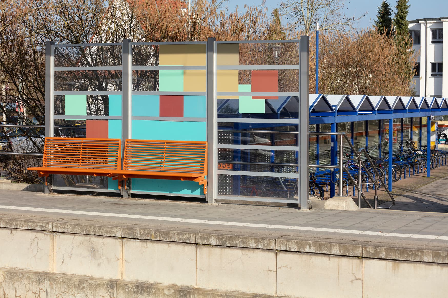 Blick auf orangefarbene Sitzbänke. Im Hintergrund ist ein überdachter Fahrradparkplatz zu erkennen.