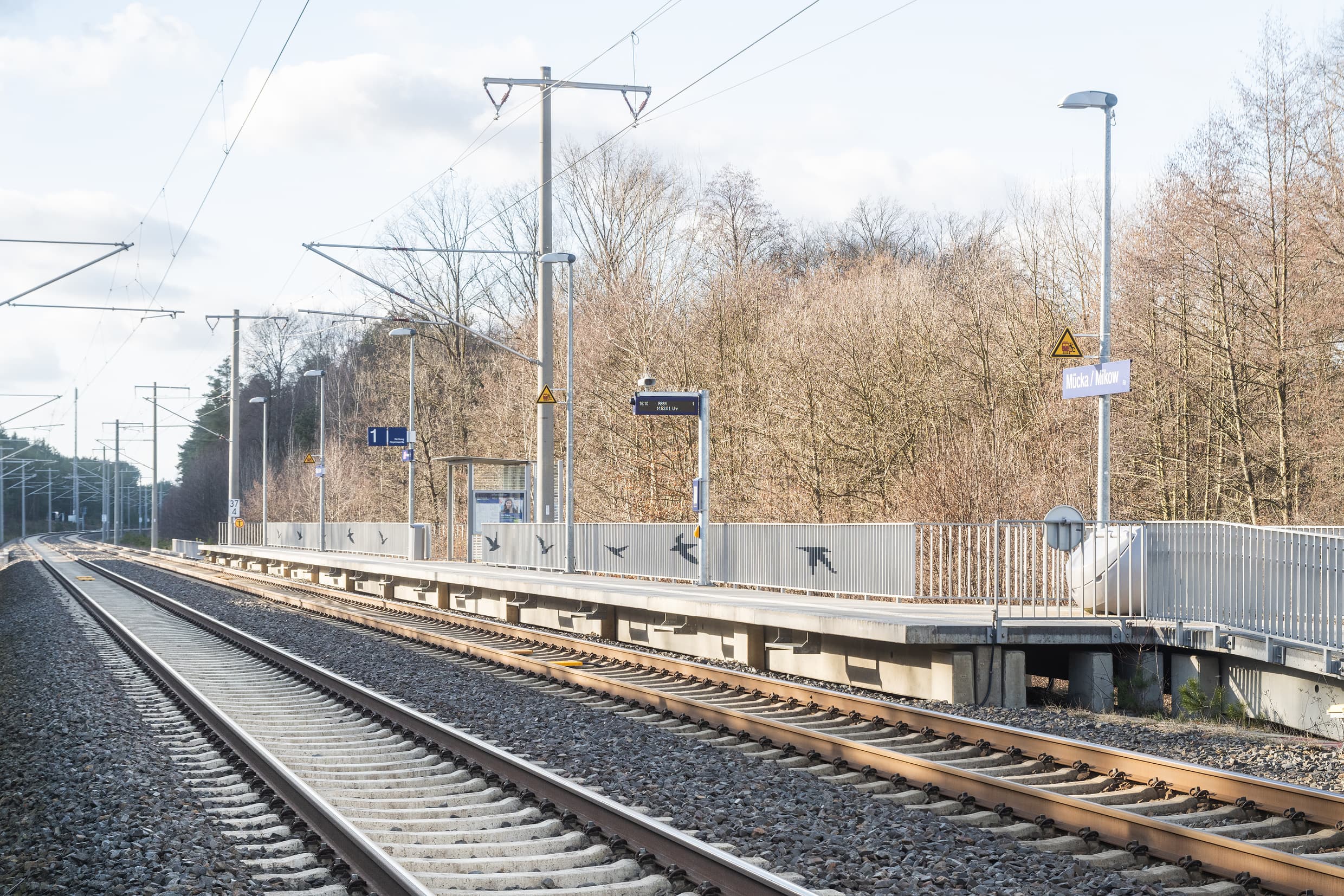 Blick auf zwei Bahngleise. Im Hintergrund ein Bahnsteig mit Geländer.