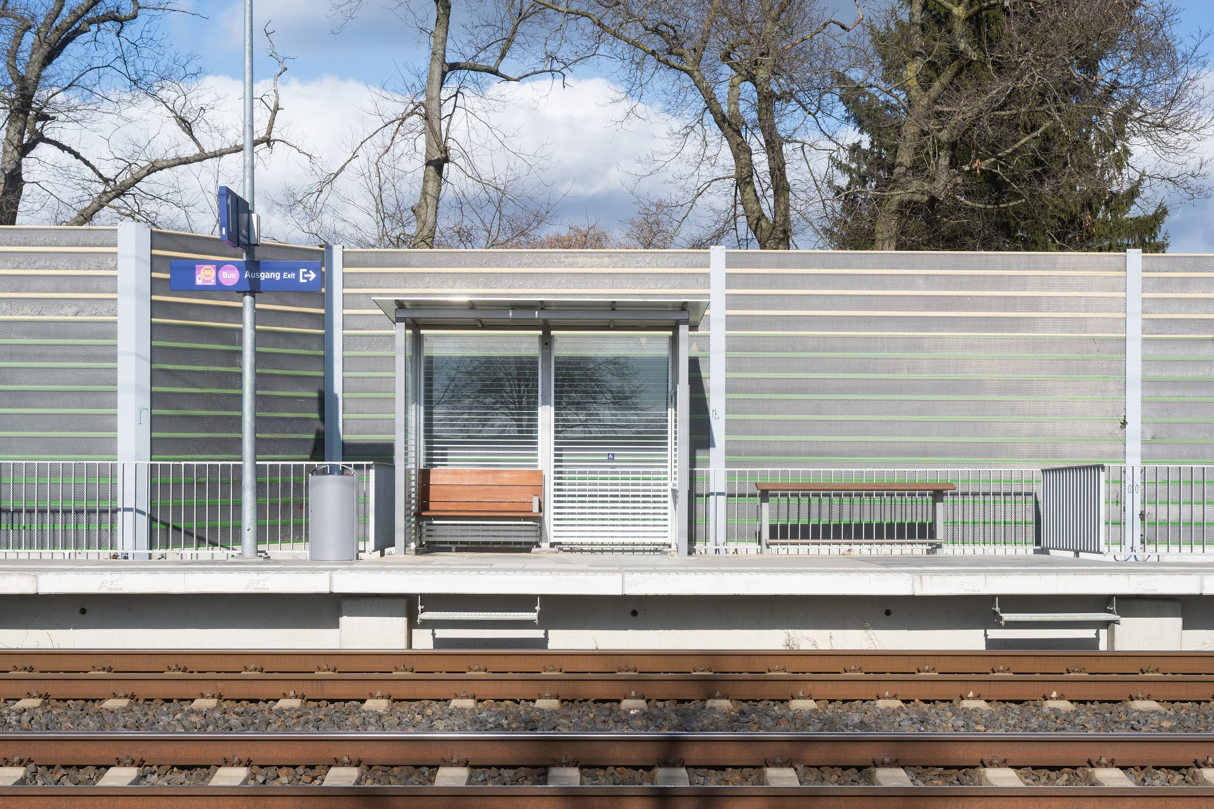Blick auf das voll transparentes Wetterschutzhaus, das vor der Schallschutzwand platziert ist.