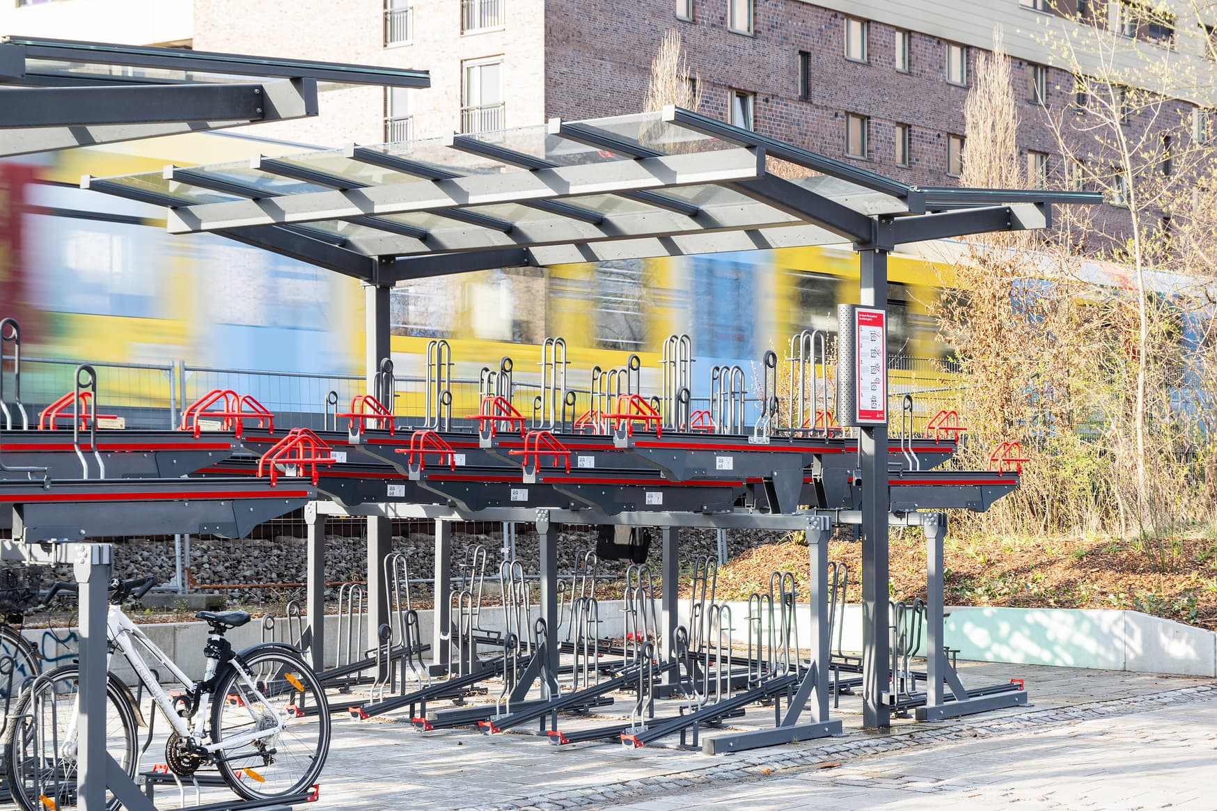 Blick auf moderne Fahrradständer. Im Hintergrund fährt ein Zug.