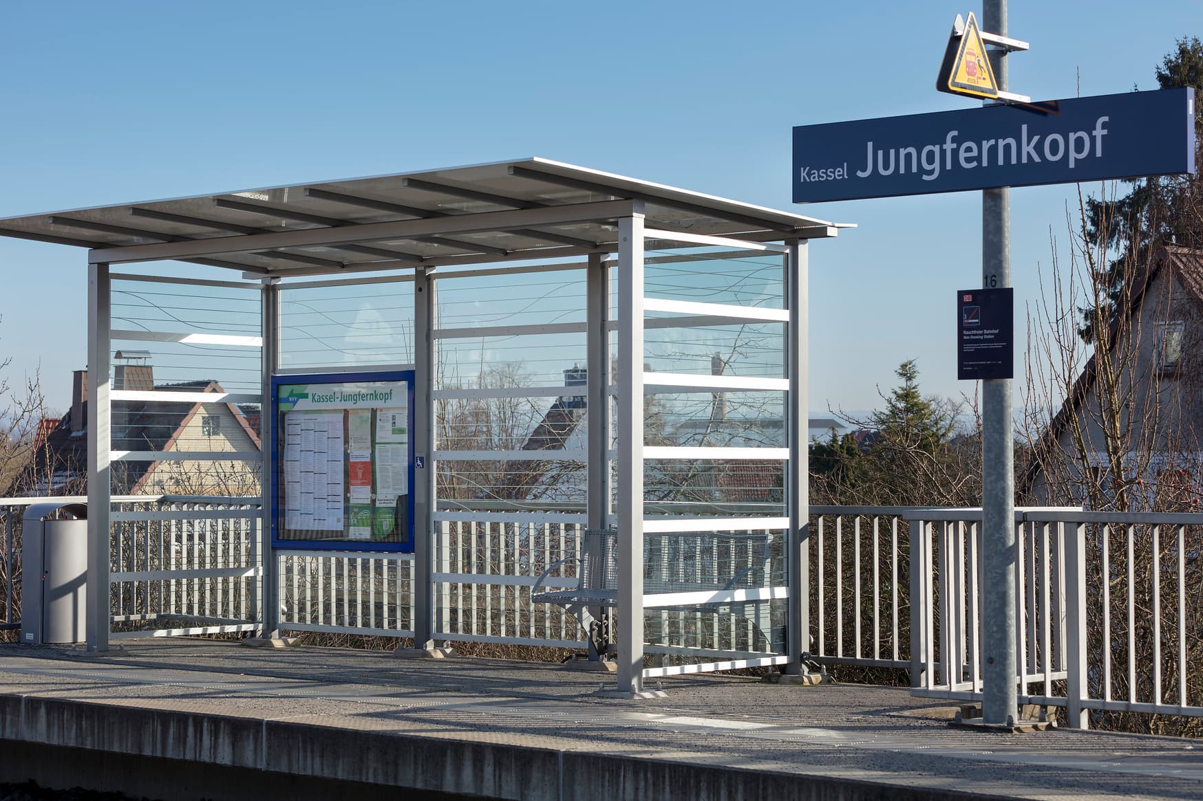 Blick auf den Bahnsteig. Links ein lichtdurchlässiges Wetterschutzhäuschen mit Sitzbank. Rechts befindet sich das Gleis.