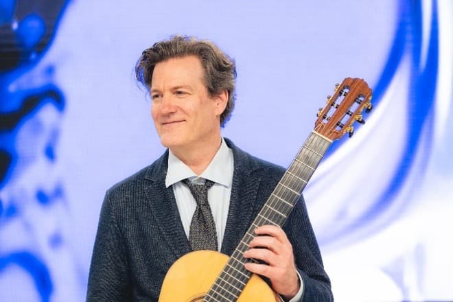  Andreas Paolo Perger mit Gitarre vor einer Projektion der Videokunst.