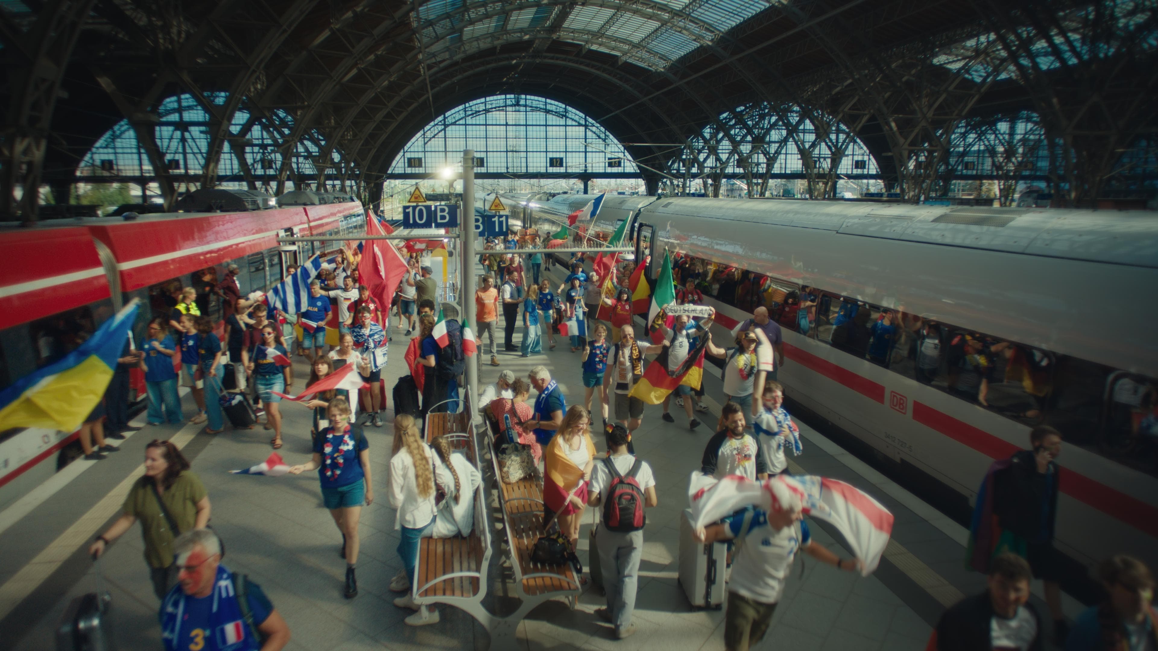 Fußballfans mit Fahnen laufen am Bahnhof über den Bahnsteig.