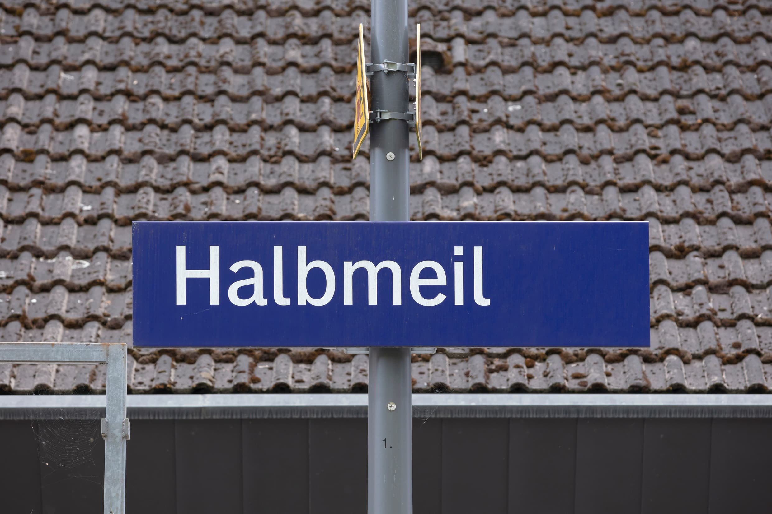 Blaues Bahnhofsschild mit weißem Schriftzug Halbmeil.