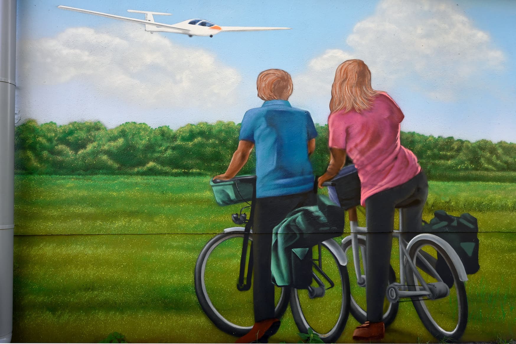 Ein bemaltes Nebengebäude des Bahnhofs zeigt zwei Radfahrer in grüner Umgebung mit Feld und Bäumen.