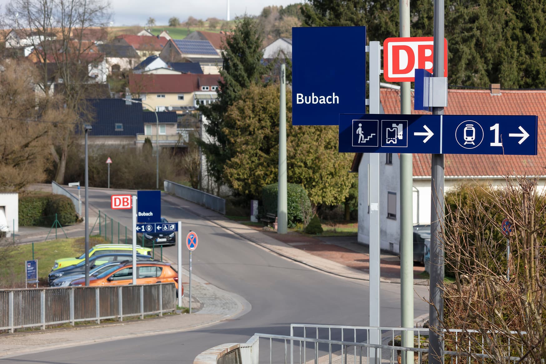Zwei Bahnhofsfahne im neuen Design mit Beschilderung zum Bahnsteigzugang, einmal im Vordergrund zur Treppe und weiter im Hintergrund beim barrierenfreien Zugang.