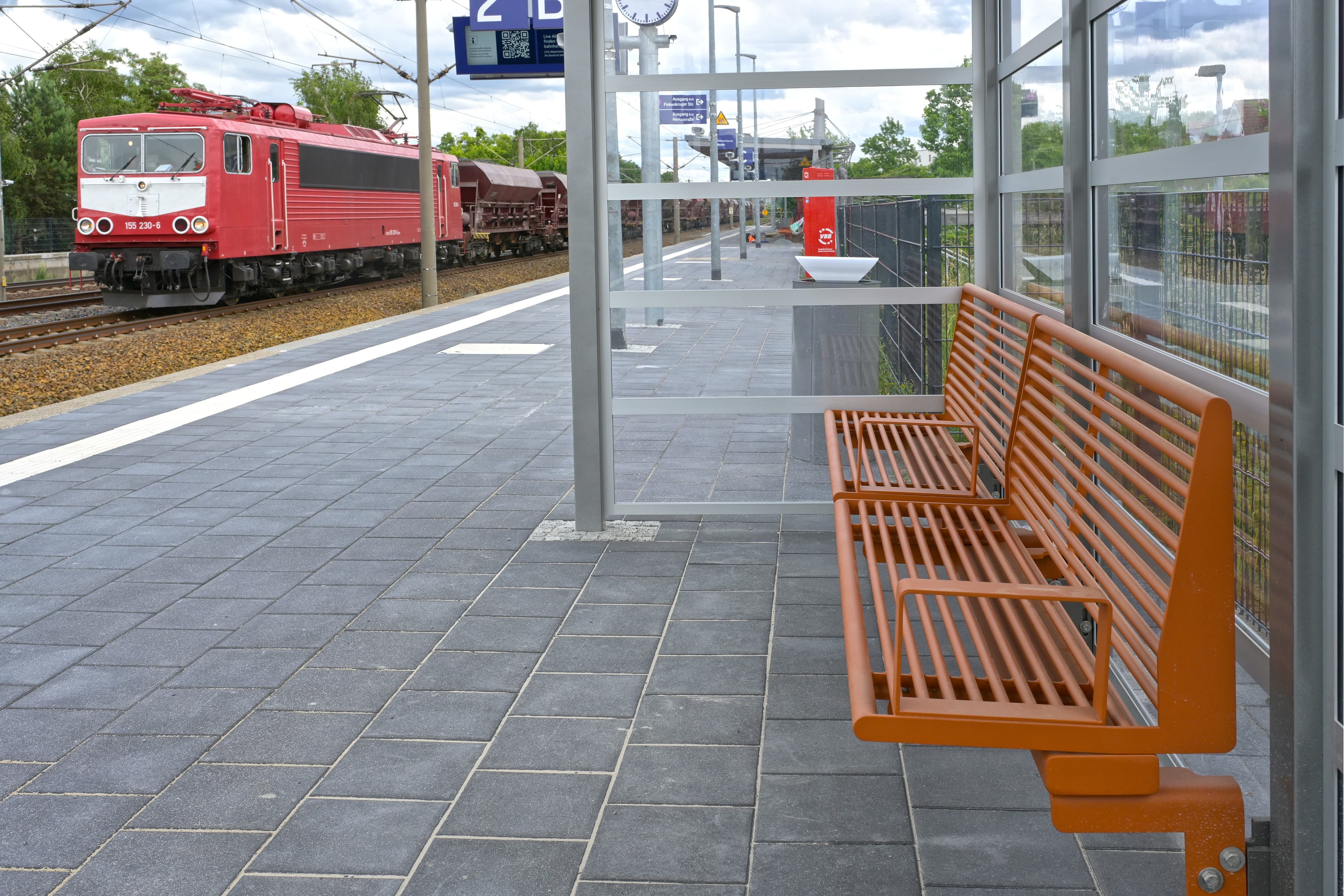 Orange Sitzbänke in einem Wetterschutzhaus an einem Bahnsteig.