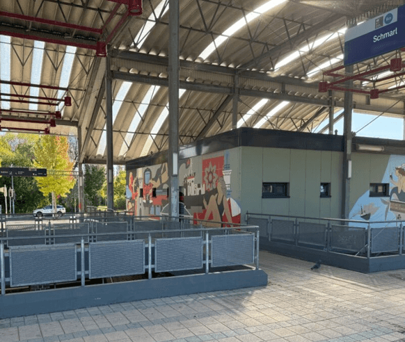 Blick auf ein Gebäude unter dem Bahnhofsvordach, in dem Läden untergebracht sind. Auf den grünen Wänden sind nun farbenfrohe Murales zu sehen. Sie zeigen maritime Motive in klarem Stil.