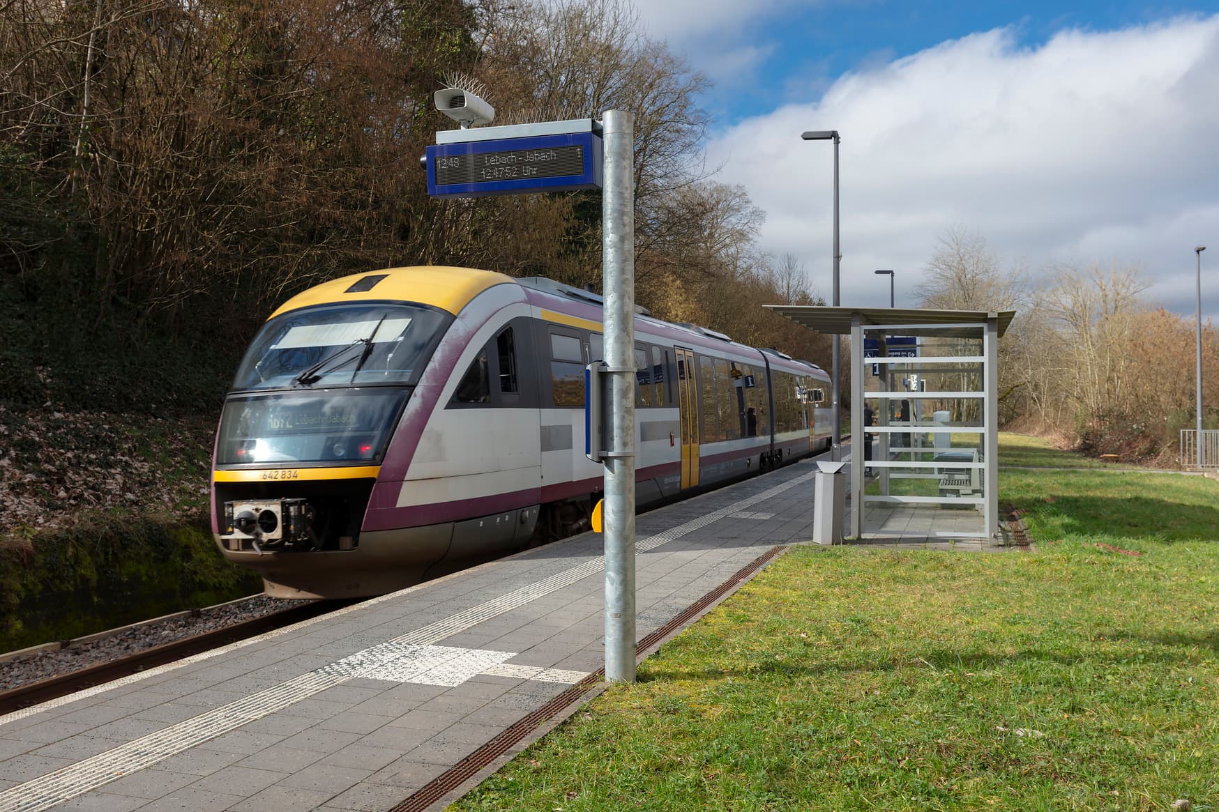 Einfahrender Zug am Bahnsteig mit taktilem Bodenleitsystem und Aufmerksamkeitsfeld vor dem Dynamischen Schriftenanzeiger Plus mit Akkustikmodul und Taster zur Sprachausgabe.