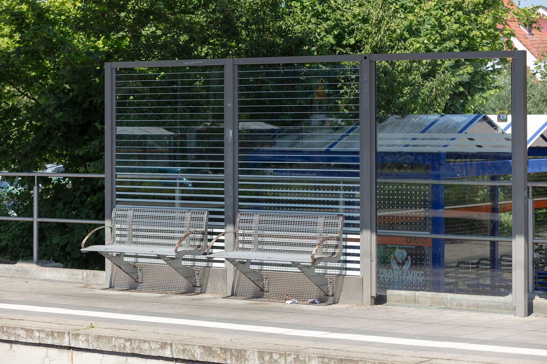 Blick auf zwei graue Sitzbänke auf einem Bahnsteig.