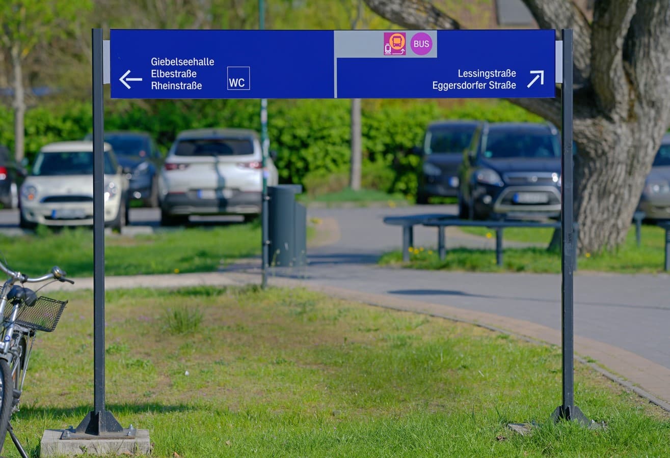 Bahnhofsvorplatz mit Wiese, Beschilderung und parkenden Autos.