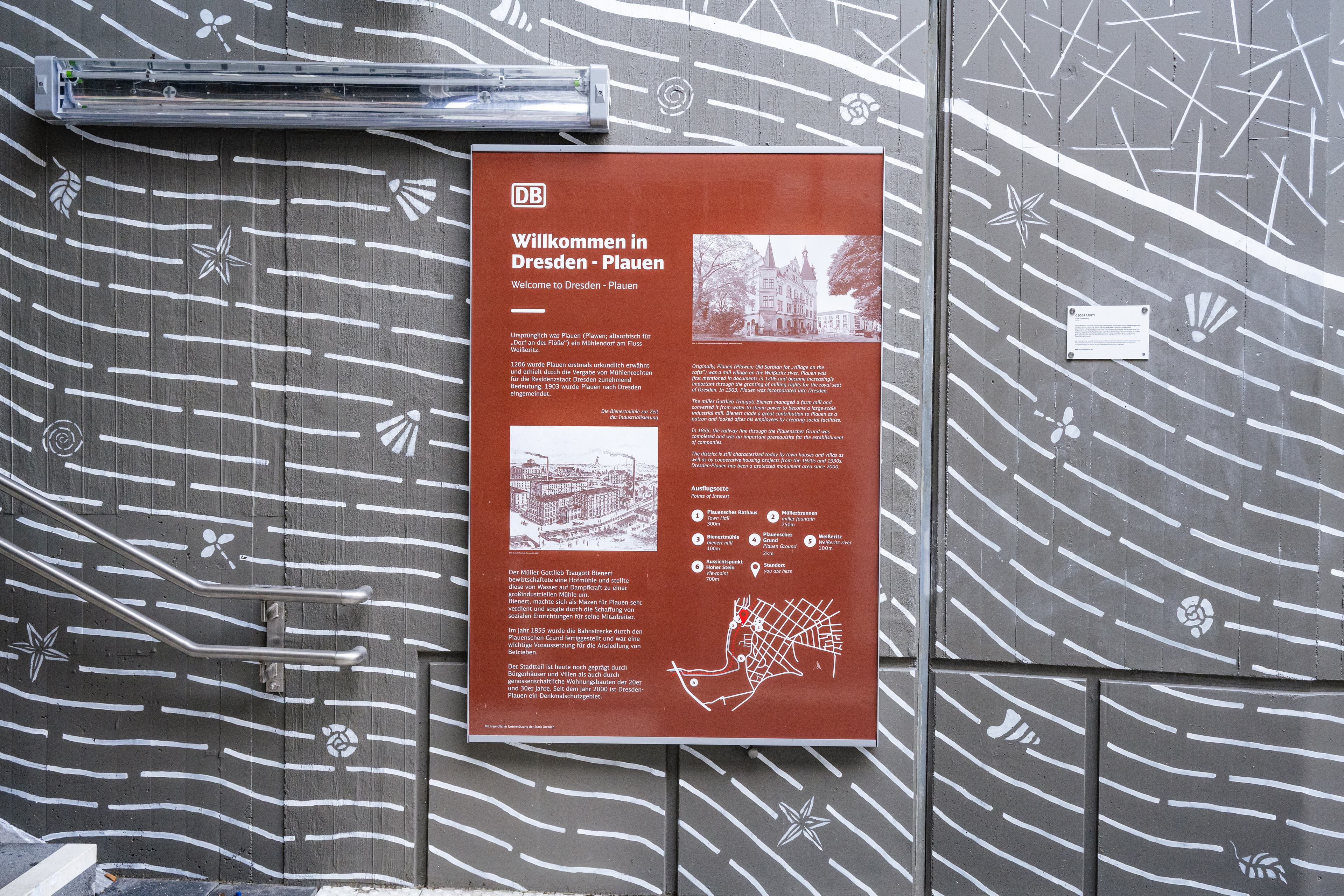 Ein braunes Board mit regionalen Information mit der gestalteten Wand im Hintergrund