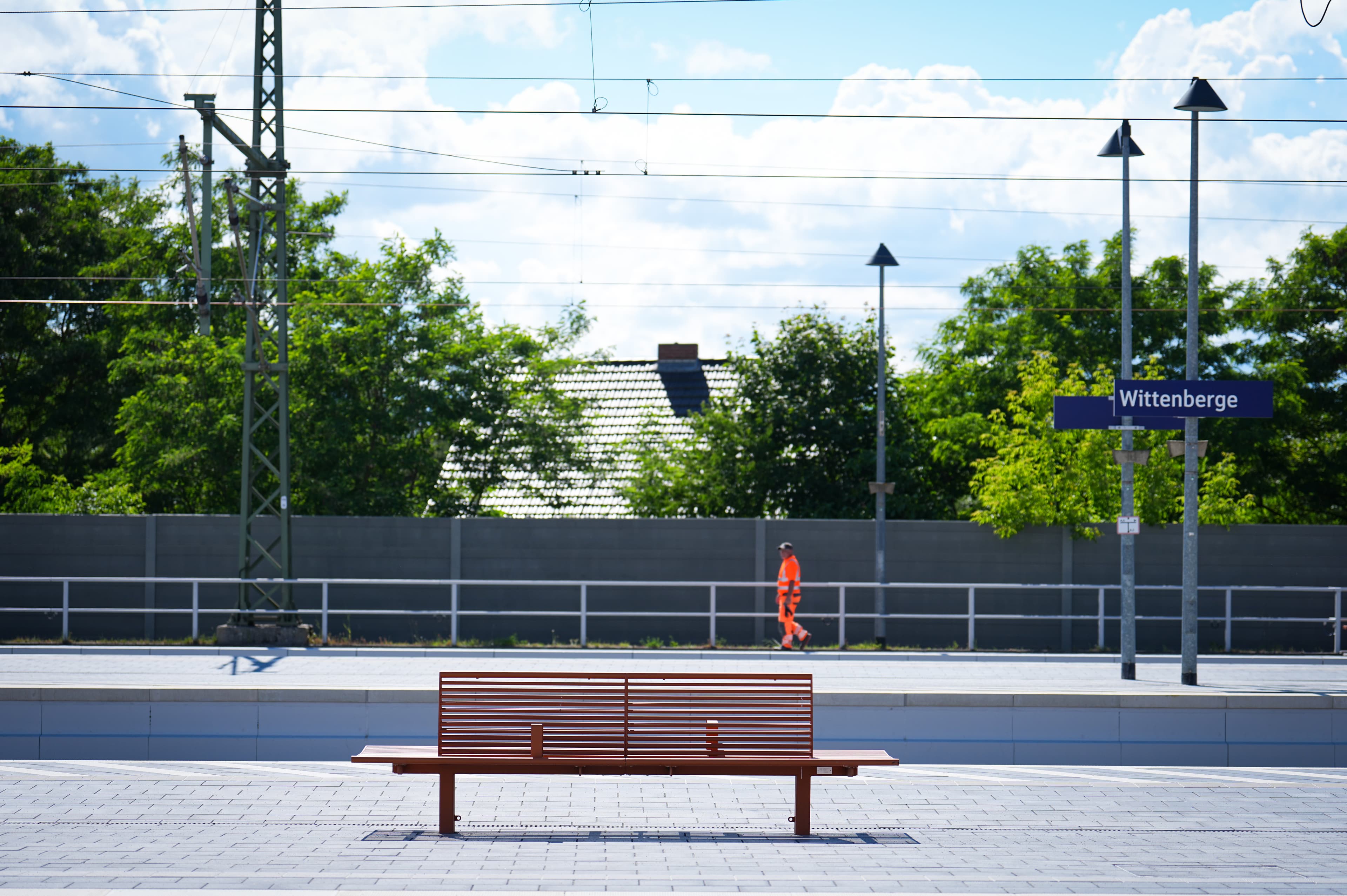 Eine orangene Sitzbank auf einem Bahnsteig.