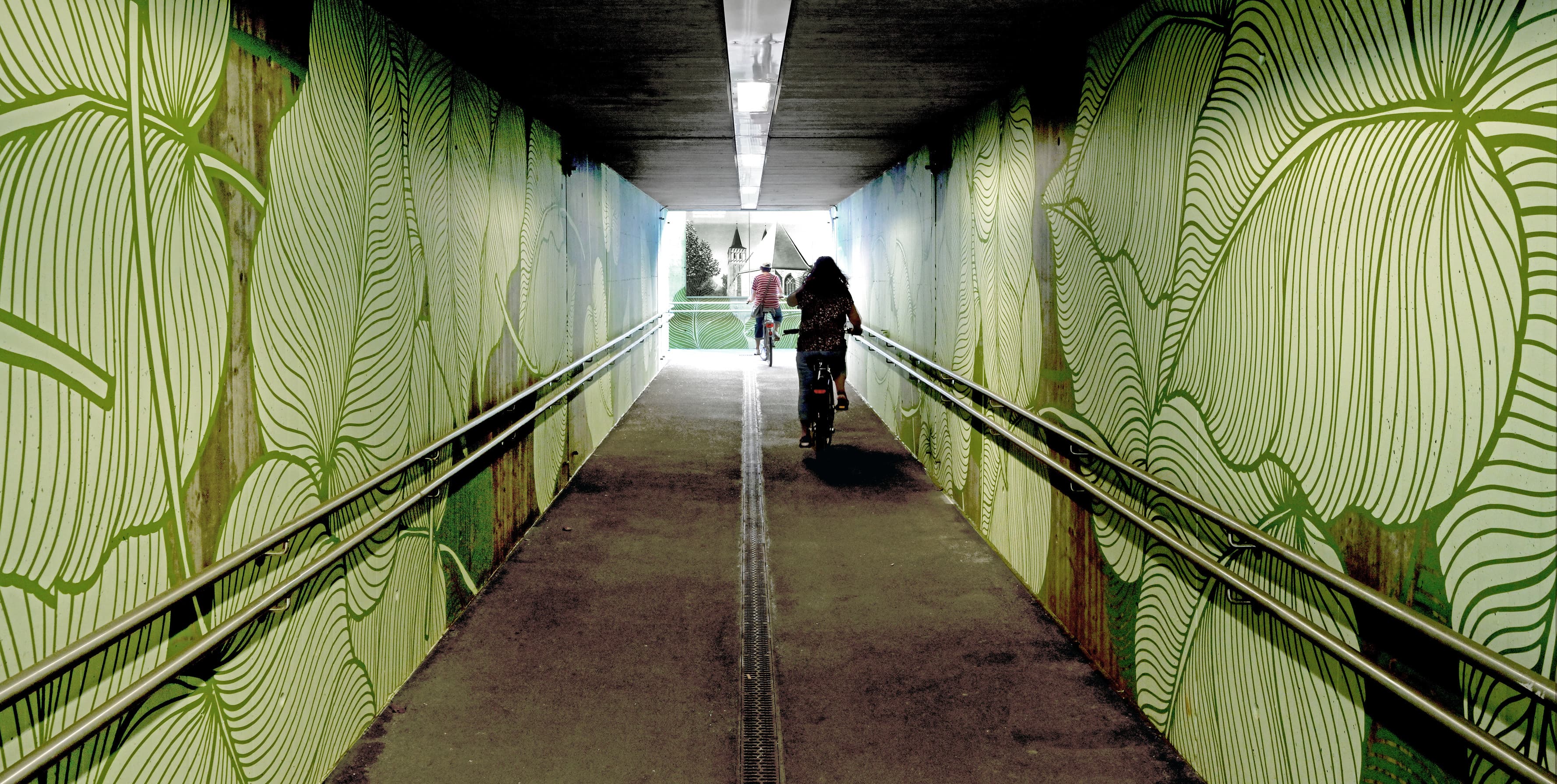 Eine Personenunterführung mit grünen Blattmustern an beiden Wänden. 