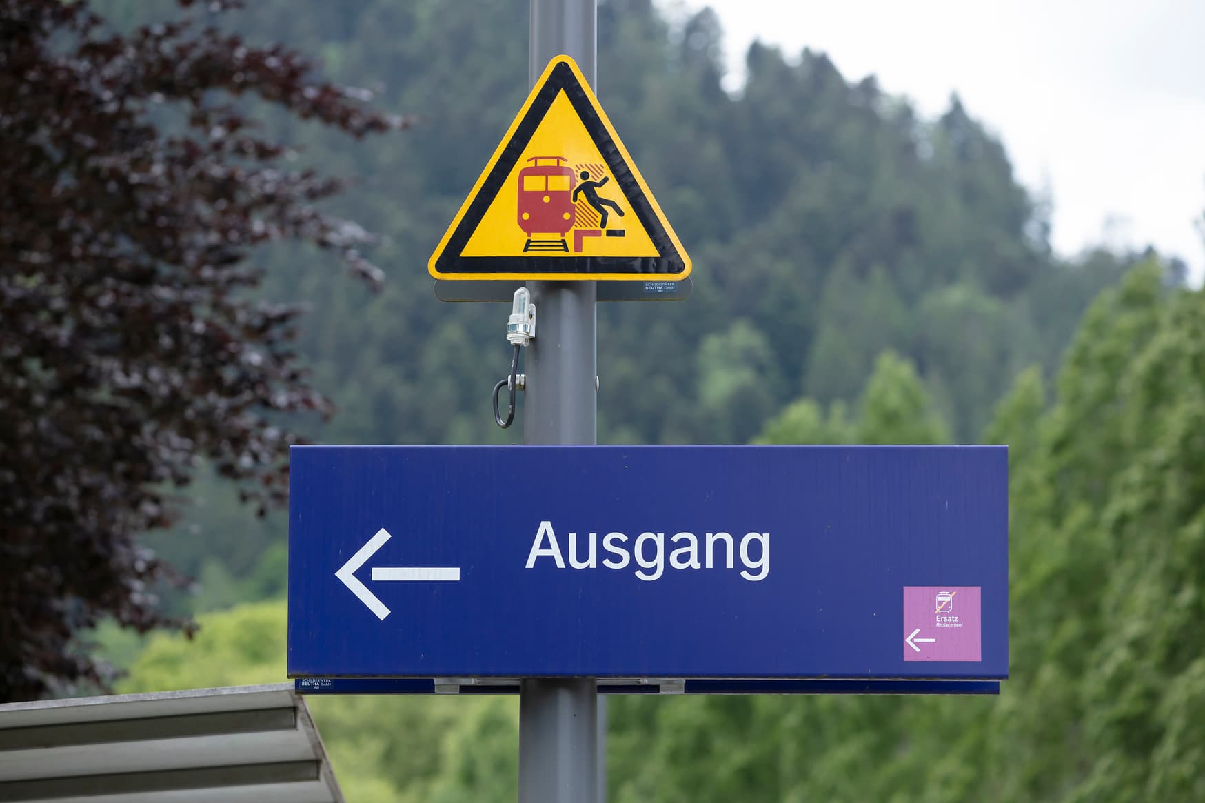 Detailaufnahme von einem blauen Schild mit dem weißen Aufdruck Ausgang, links im blauen Schild das Piktogramm vom Schienenersatzverkehr mit Pfeilrichtung.