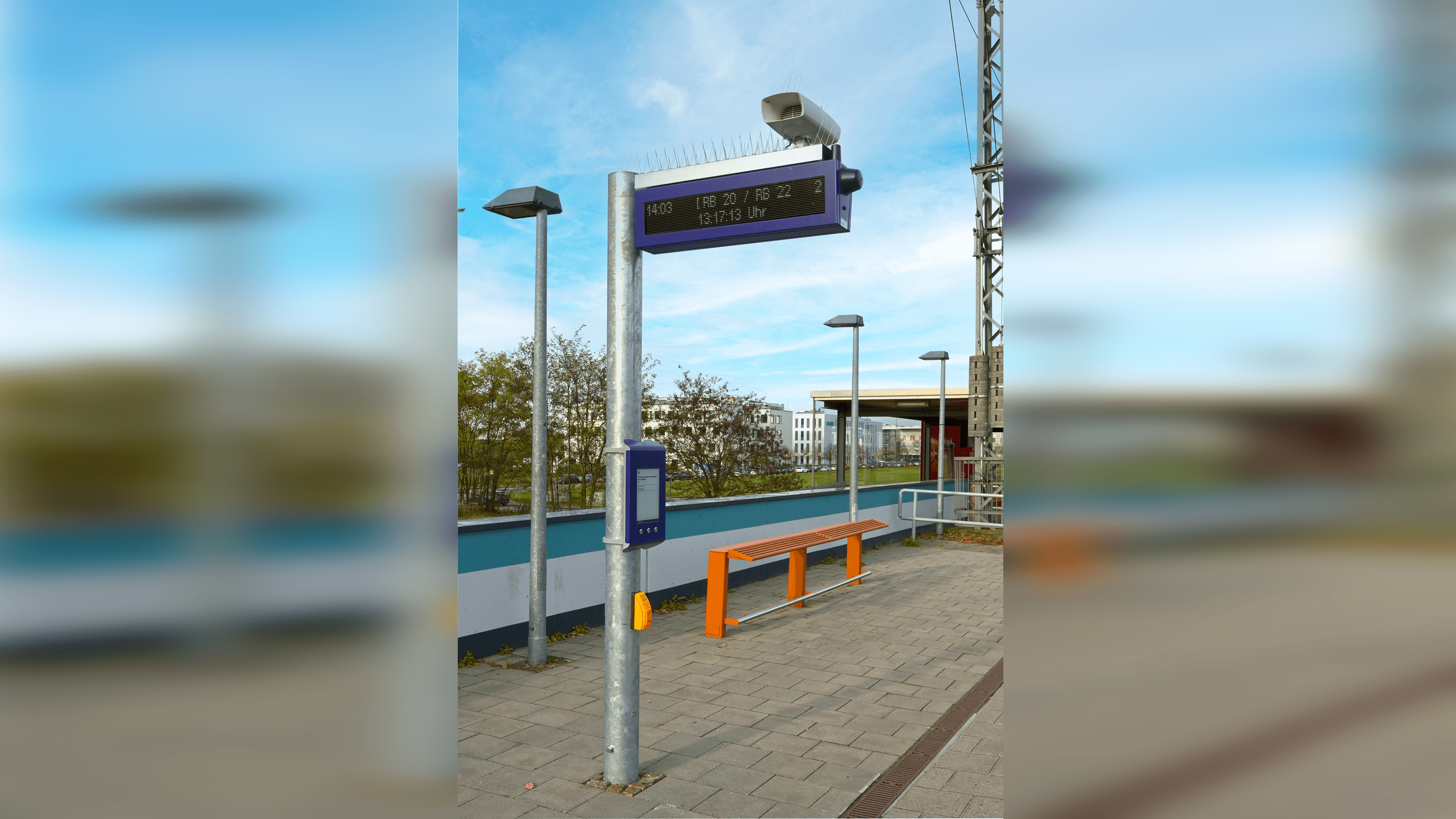 Zu sehen ist ein Dynamischer Schriftenanzeiger Plus. Ganz oben an dem Mast befindet sich ein Display mit aktuellen Reiseinformationen und ein Lautsprecher. Darunter hängen der Digitale Aushang Baukommunikation und ein Taster für die Sprachausgabe aktueller Informationen.