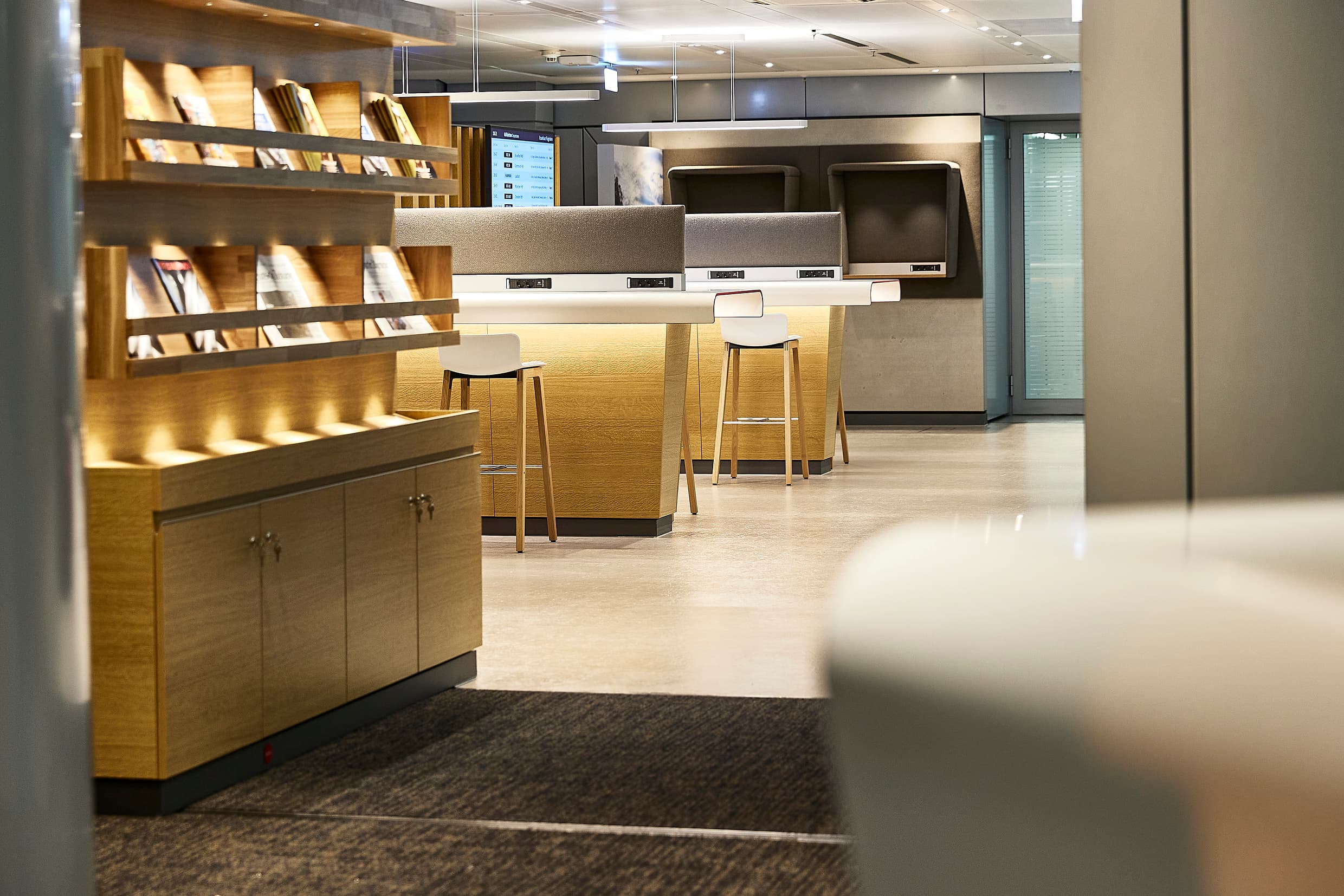 Ein beleuchtetes Regal mit Zeitschriften dahinter stehen Hochtische zum Arbeiten.