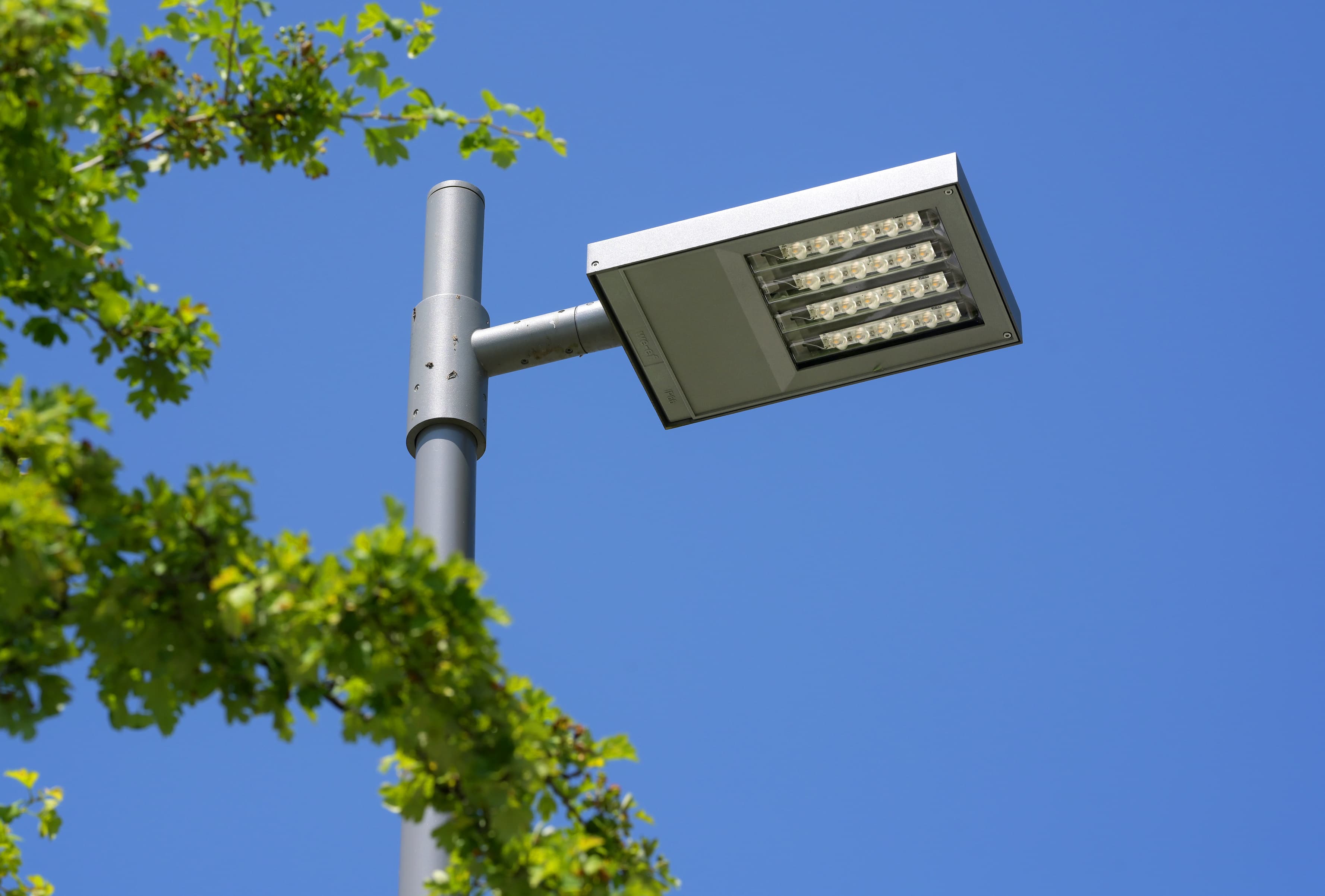 Ein moderner LED-Strahler befestigt an einem Masten vor wolkenfreiem Himmel.