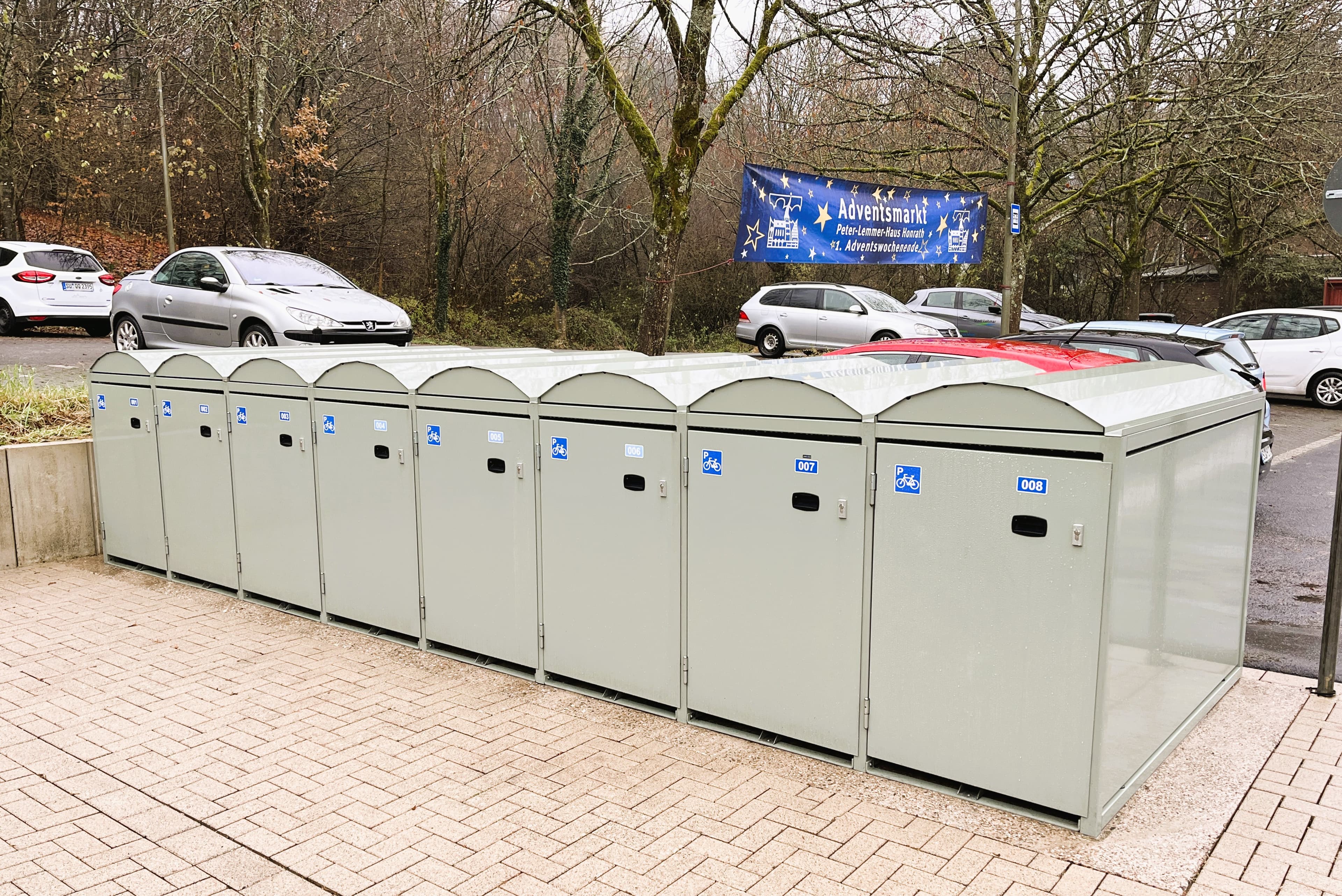 Blick auf Fahrradboxen. Dahinter sind parkende Autos zu sehen.