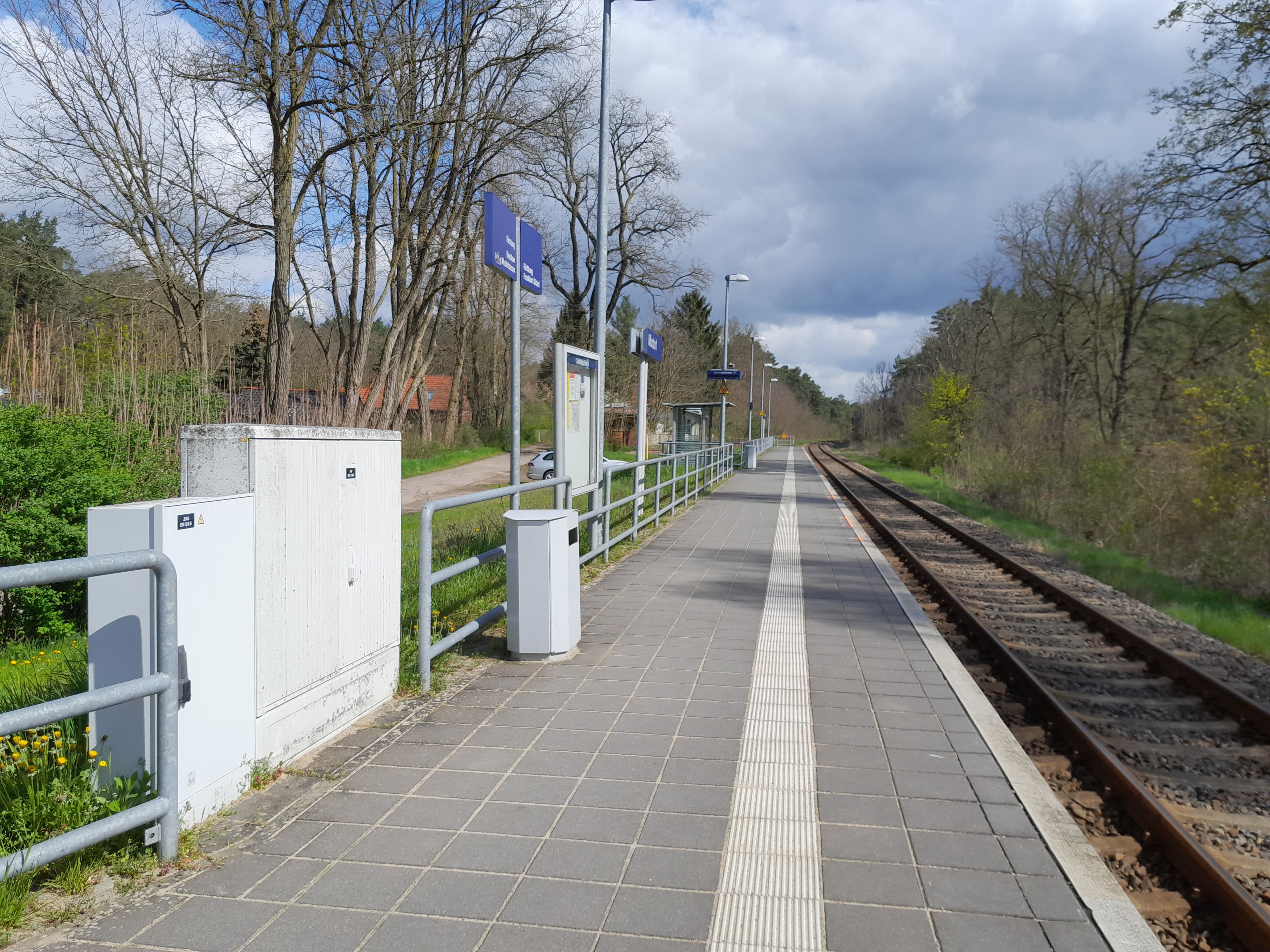 Ein Bahnsteig mit Stromkasten, Mülleimer, Vitrine und Schilder, rechts Gleise.