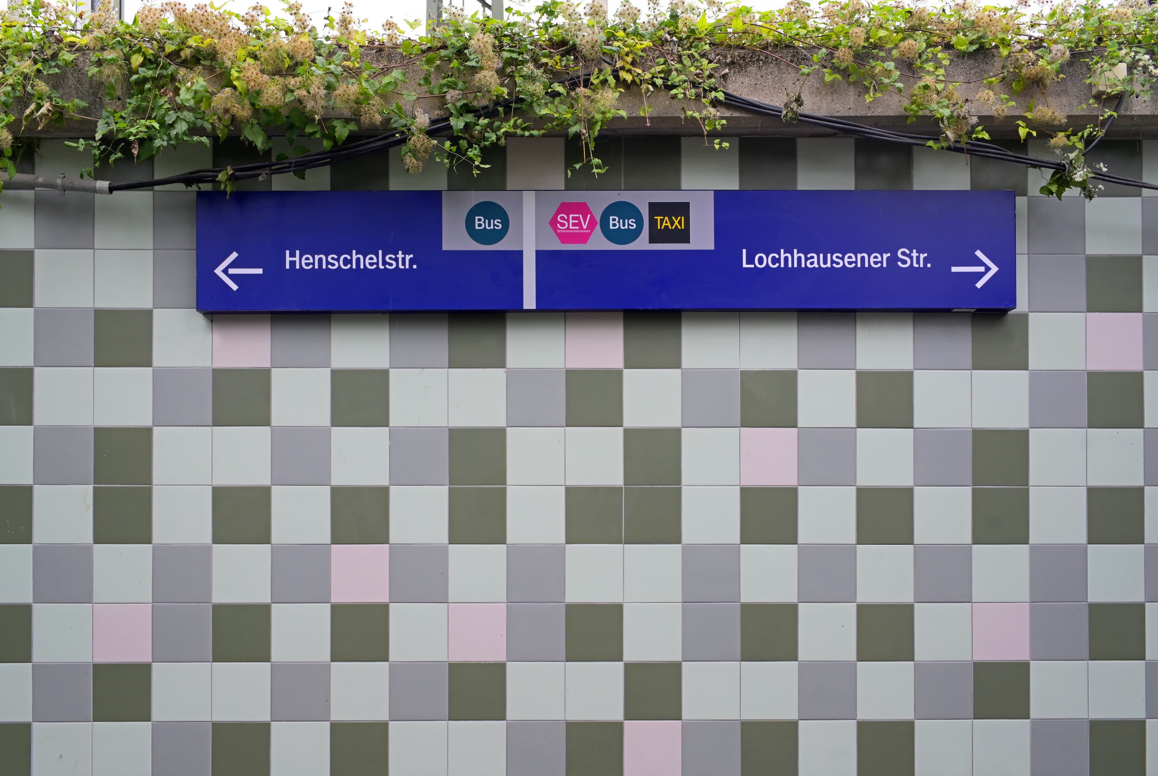 Frontale Sicht auf die neu geflieste Wand in der Personenunterführung. Zu sehen sind zudem die neuen Hinweisschilder zu den beiden Ausgängen Henschelstr. und Lochhausener Str.
