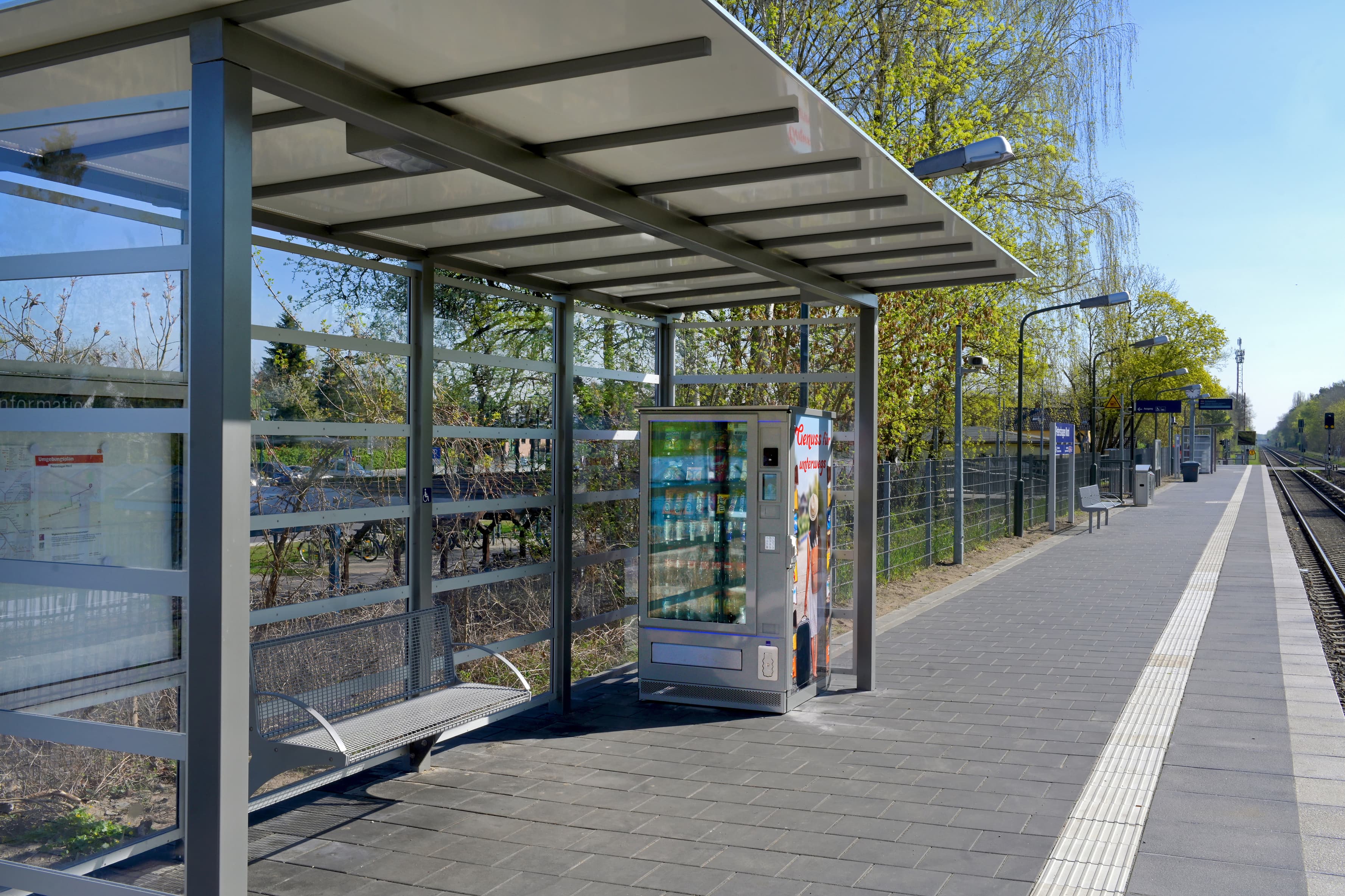 Ein Wetterschutzhaus mit Glaselementen und einem Getränkeautomat auf einem Bahnsteig.
