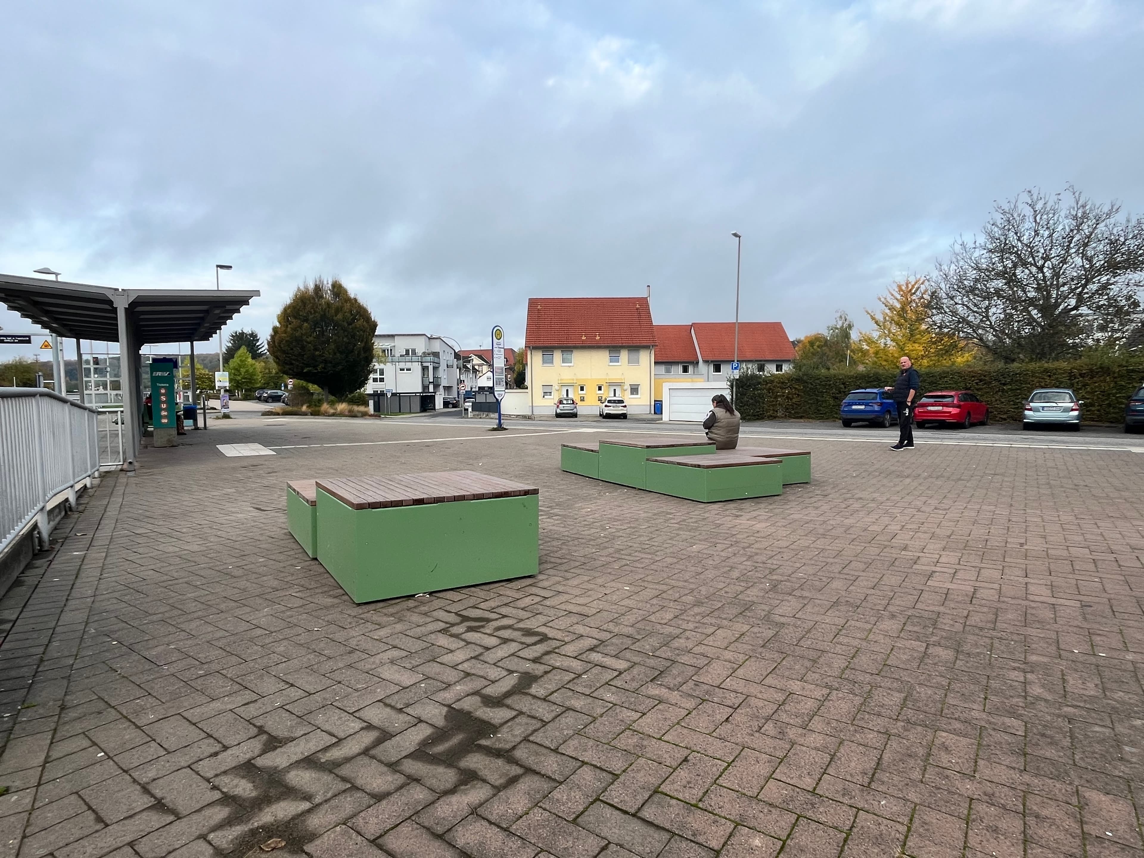 Bahnhofsvorplatz mit grünen Sitzgelegenheiten.