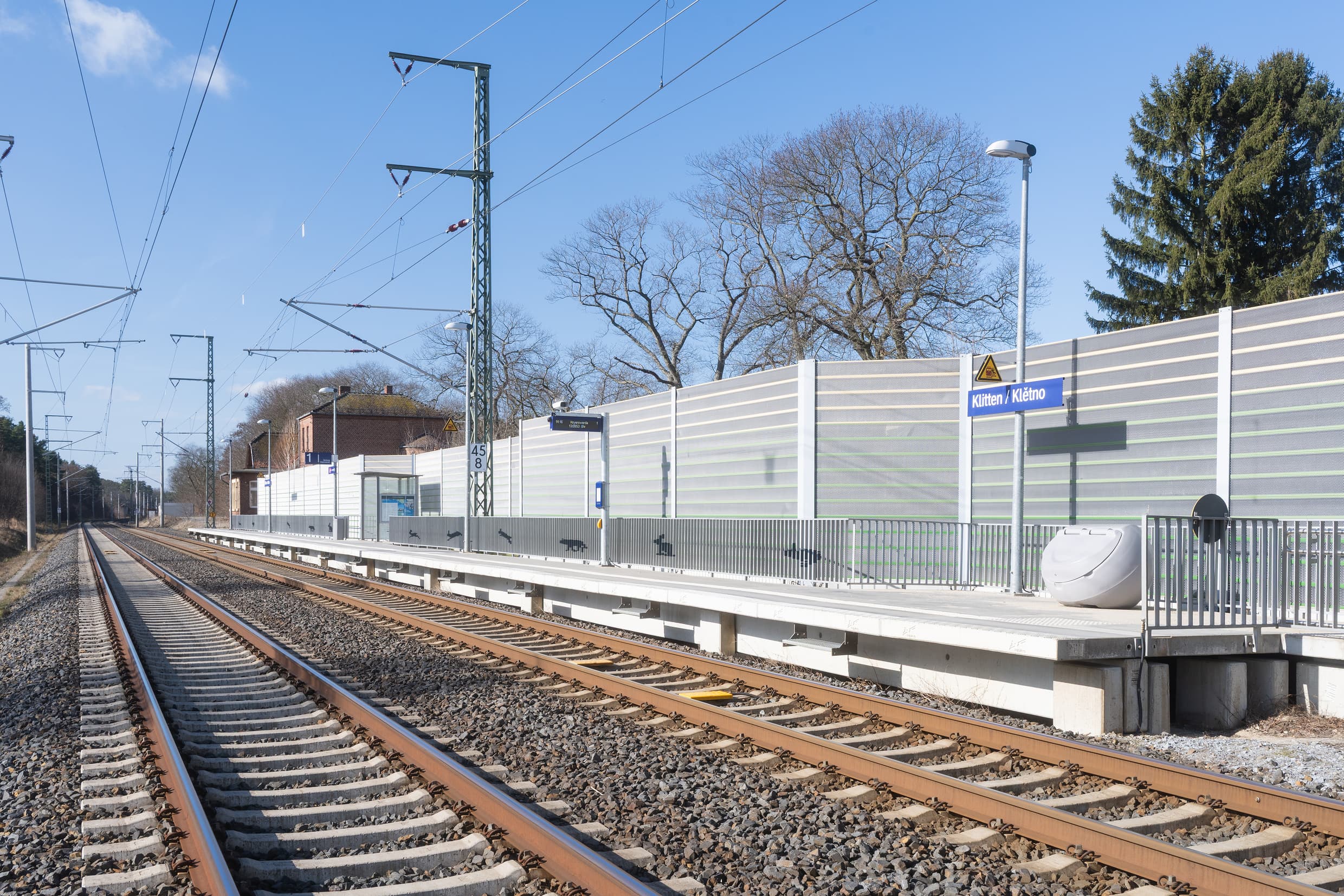 Eingleisiger Bahnsteig mit dahinterliegender grauen Schallschutzwand. Bahnsteig ist mit einem Geländer abgetrennt, welches mit Tiermotiven wie Hase und Fuchs gestaltet wurde