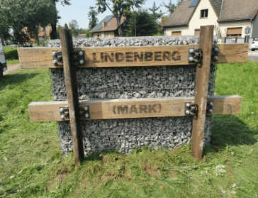 Holzplanken und Steine bilden ein Ortsschild.