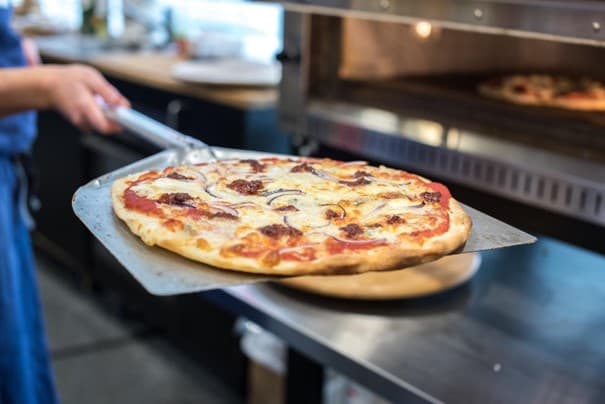 Fertige Pizza wird mit einem Backschieber aus dem Ofen geholt.
