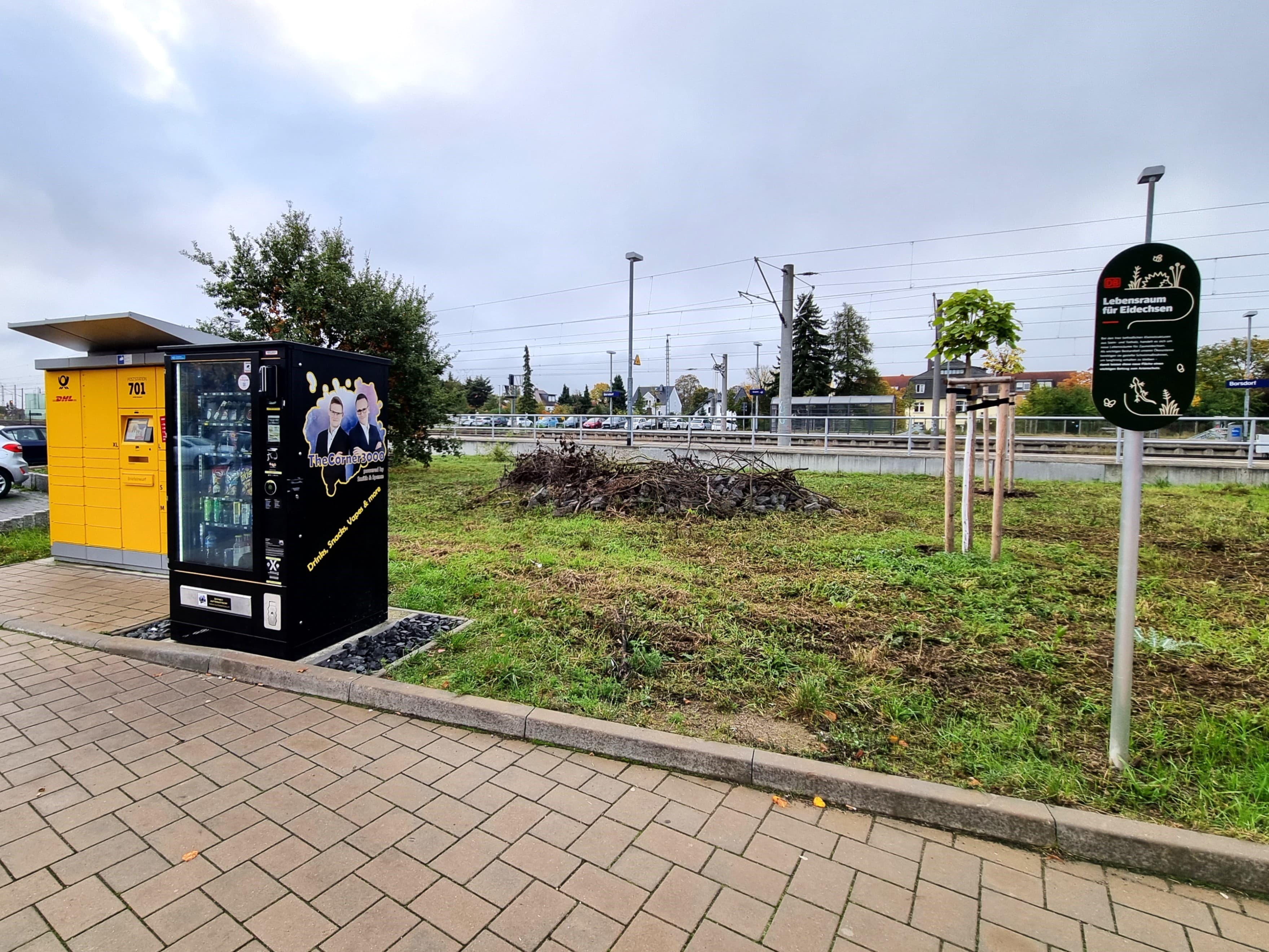 Zu sehen ist eine Paketstation und einen Waren-Automat. Beides stellte die Stadt auf. Im Hintergrund auf der Grünfläche hat die DB einen Lebensraum für Eidechsen geschaffen. 