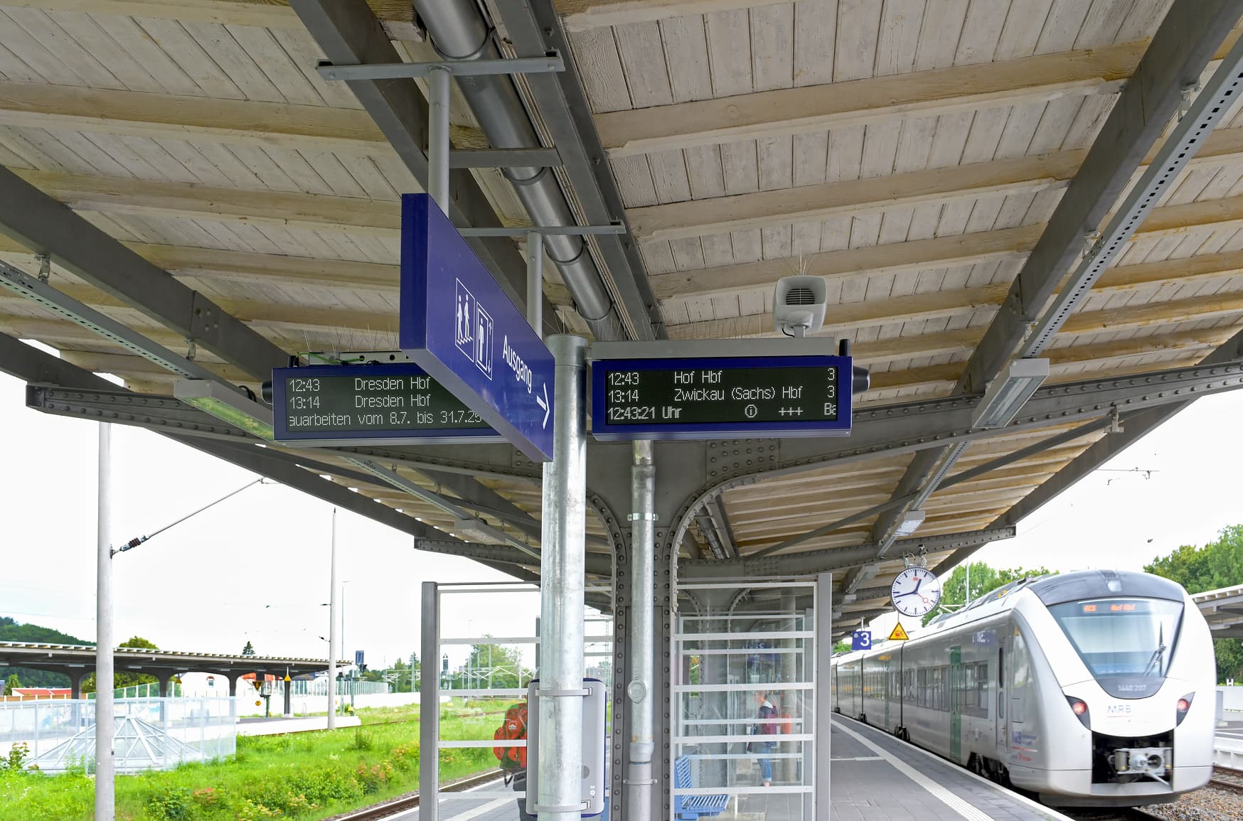Zu sehen ist das Bahnsteigdach und zwei Digitale Anzeiger mit den nächsten Abfahrtszeiten.
