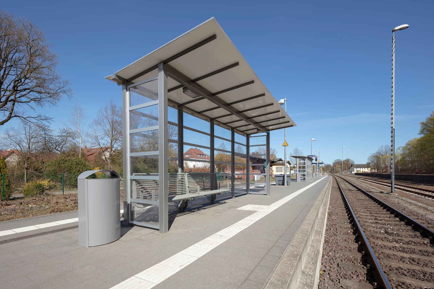 Wetterschutzhäuschen auf einem Bahnsteig. Davor sind Gleise zu sehen.