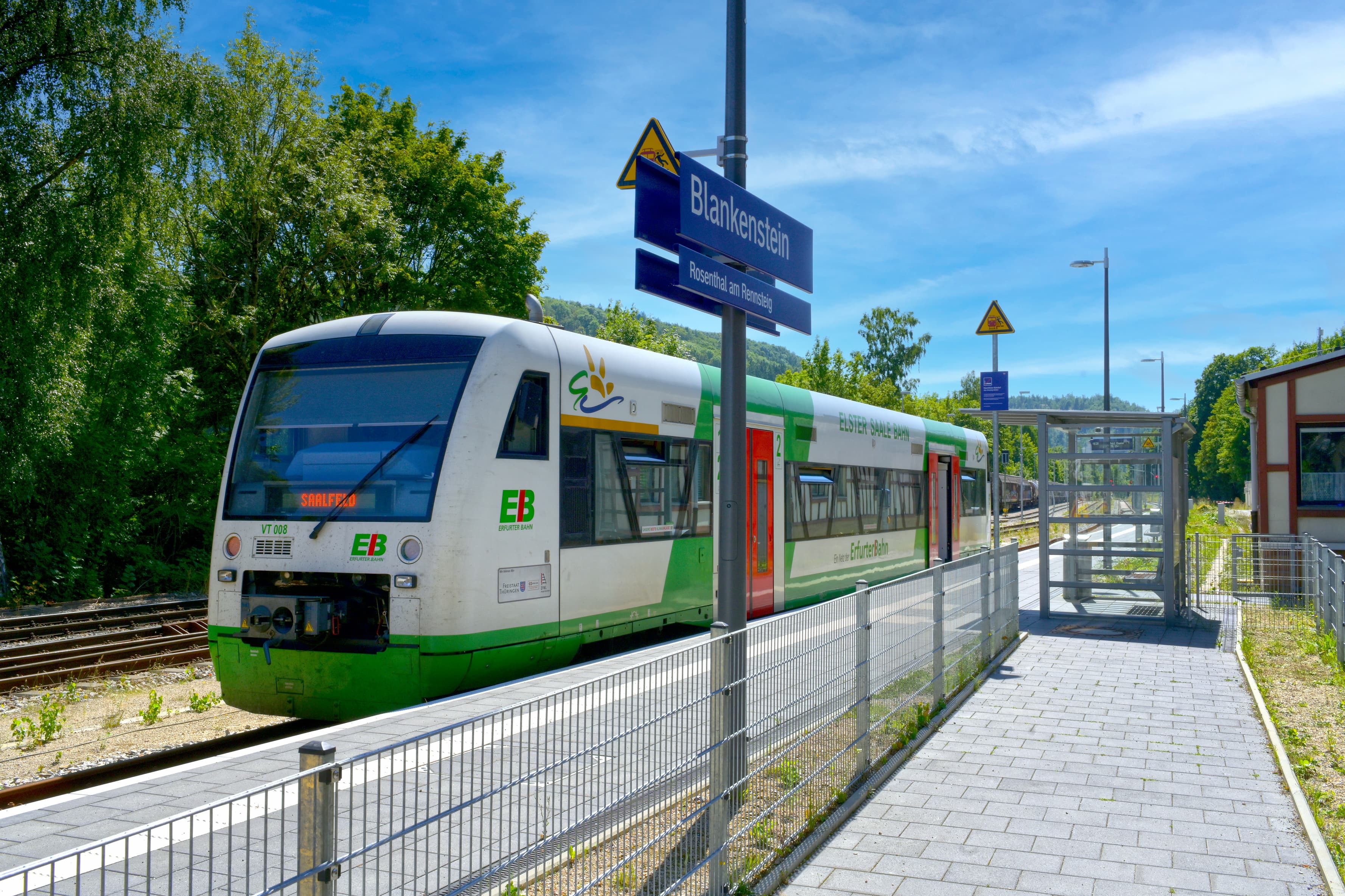 Separat gepflasterte Zuwegung für zum eingleisigen Bahnsteig. Ein Zug der Erfurter Bahn steht an Bahnhof und man sieht das volltransparente Wetterschutzhaus