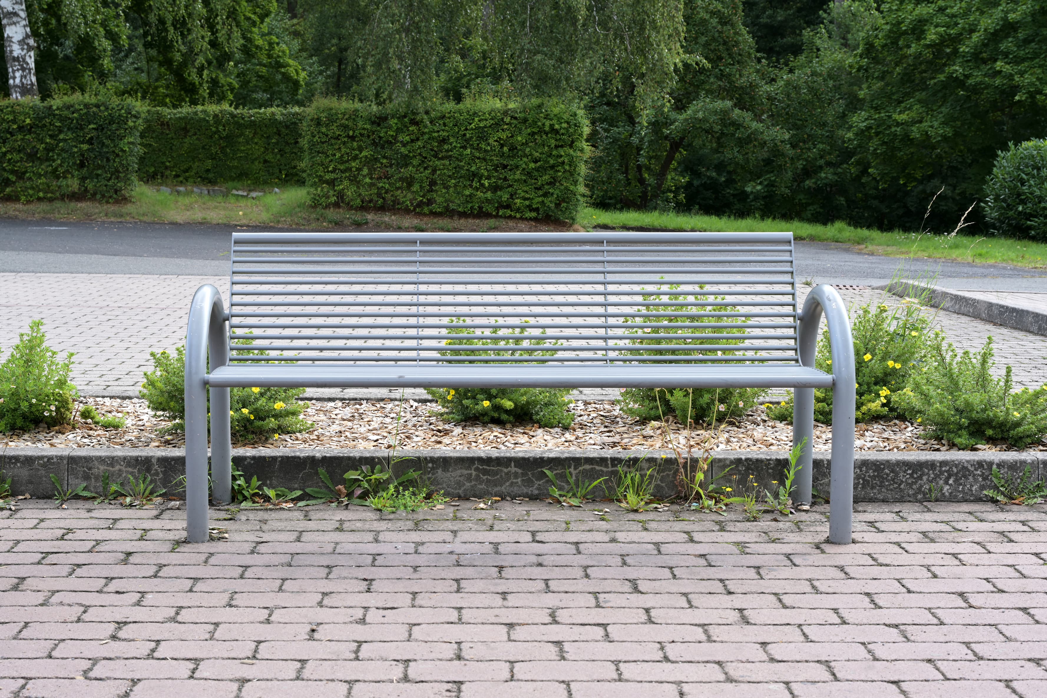 Graue Stahlbank mit Begrünung im Hintergrund auf dem Vorplatz.