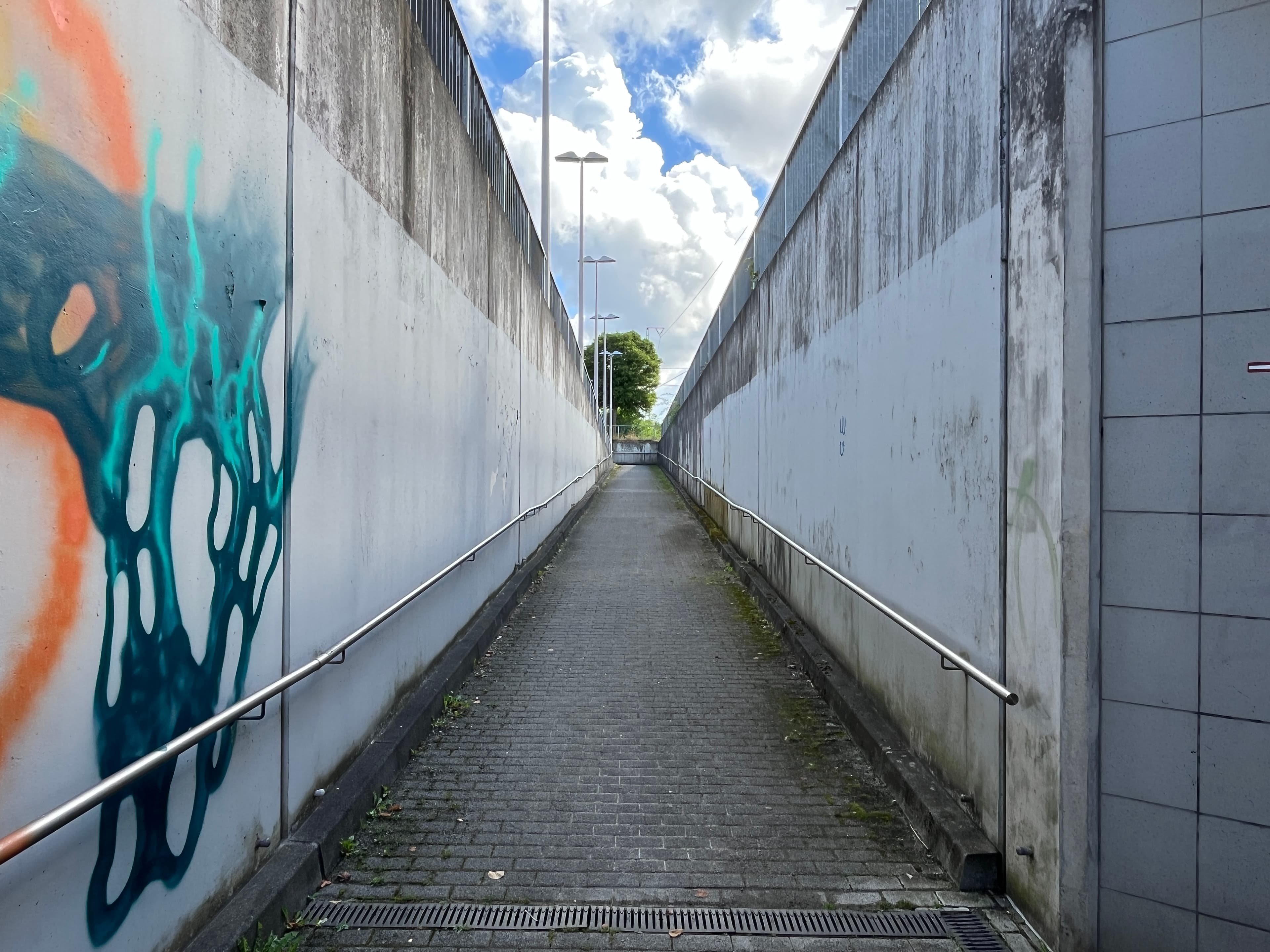 Blick auf den Aufgang einer Personenunterführung. Rechts und links davon Wände mit Handläufen.