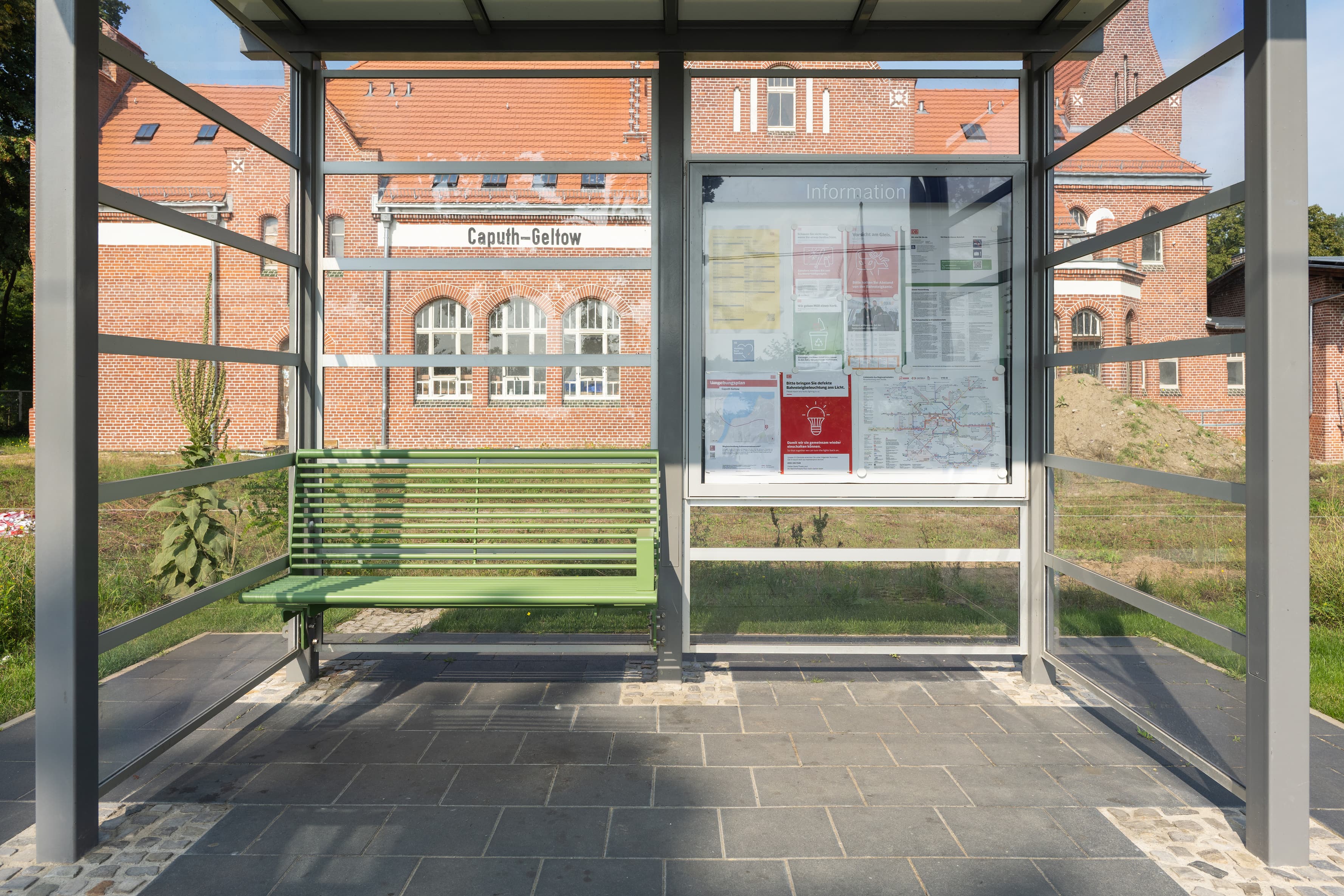 Eine grüne Sitzbank und eine Infovitrine in einem Wetterschutzhaus. 