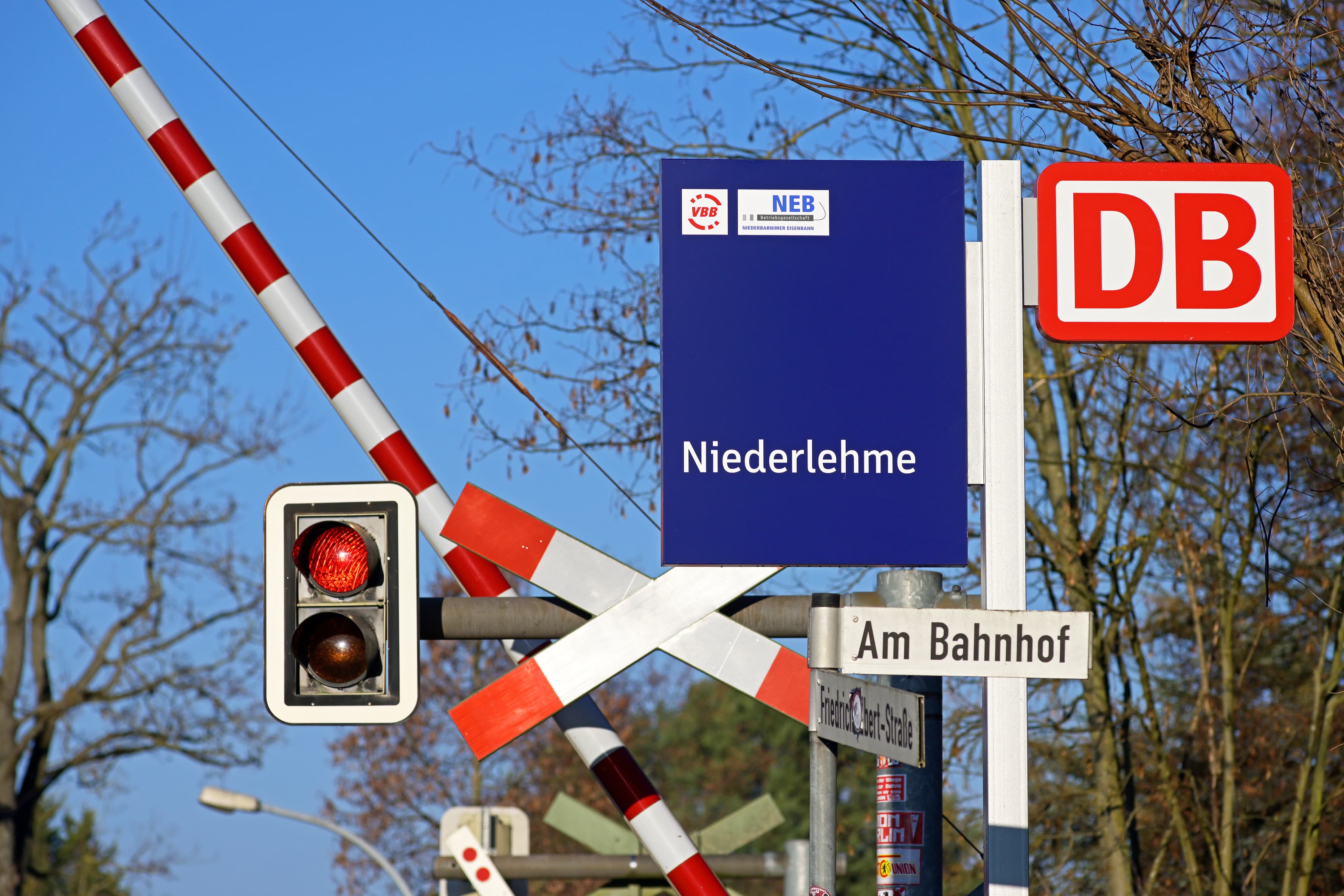 Bahnübergangsschranken und Ampel. Rechts daneben befinden sich Beschilderungen.