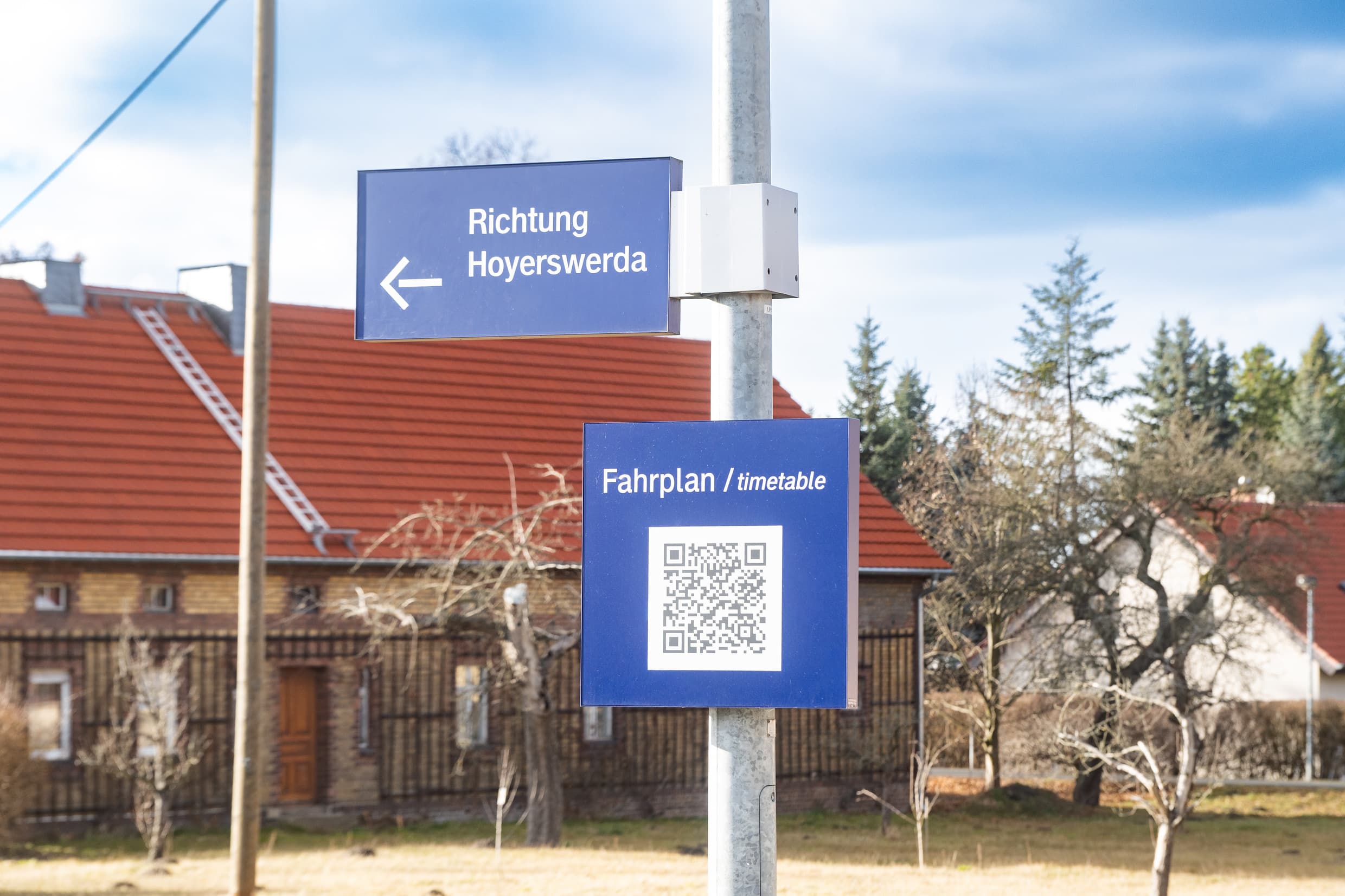 Blaues Schild mit einem QR-Code und dem Verweis auf den digitalen Fahrplan - zusätzlich sieht man noch das Richtungsschild Hoyerswerda.