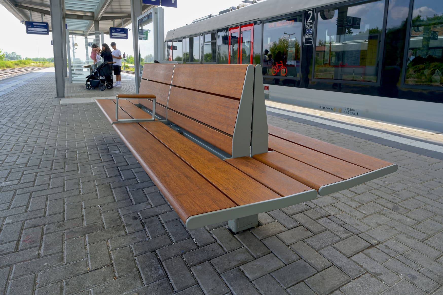 Eine Sitzbank aus Holz und Metall auf einem Bahnsteig.