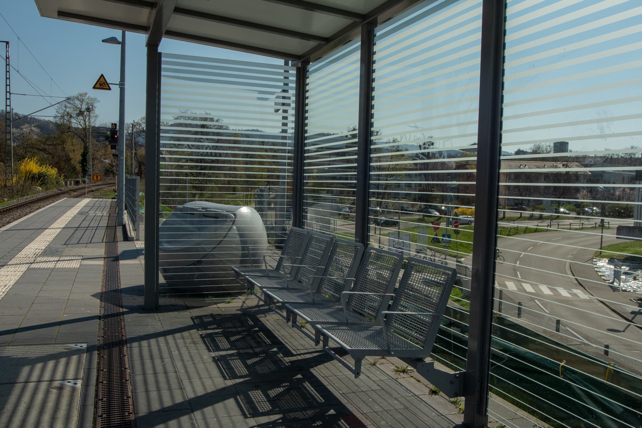 Modernes Wetterschutzhäuschen und Abfallbehälter am Bahnsteig.