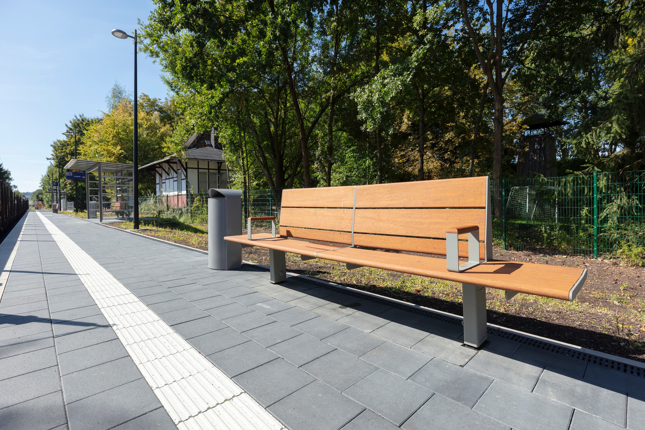 Auf dem Bahnsteig steht eine Holzbank, daneben ein Mülleimer.