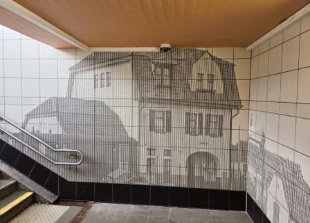 Dargestellt in Raster ein historisches Haus direkt an der Wand neben dem Treppenaufgang.