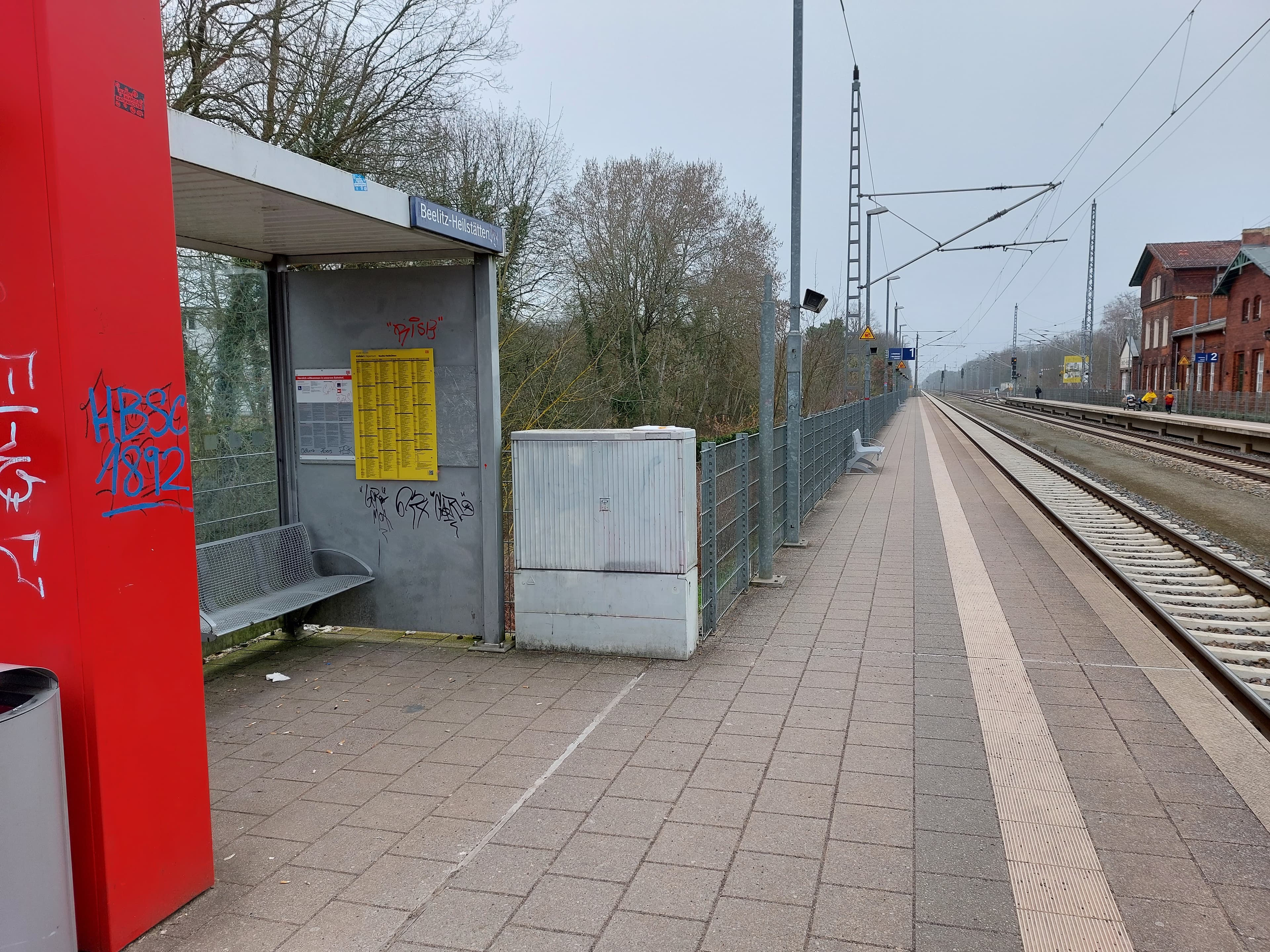 Man sieht ein mit Graffiti beschmiertes Wetterschutzhaus, die Gleise sind rechts.
