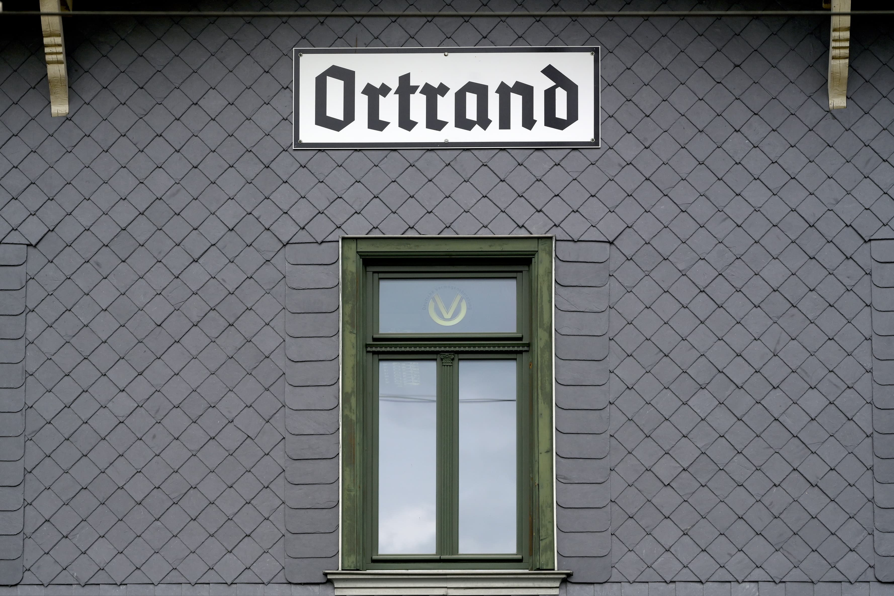 Ein Stadtschild von Ortrand auf der Schieferfassade des Bahnhofsgebäudes.