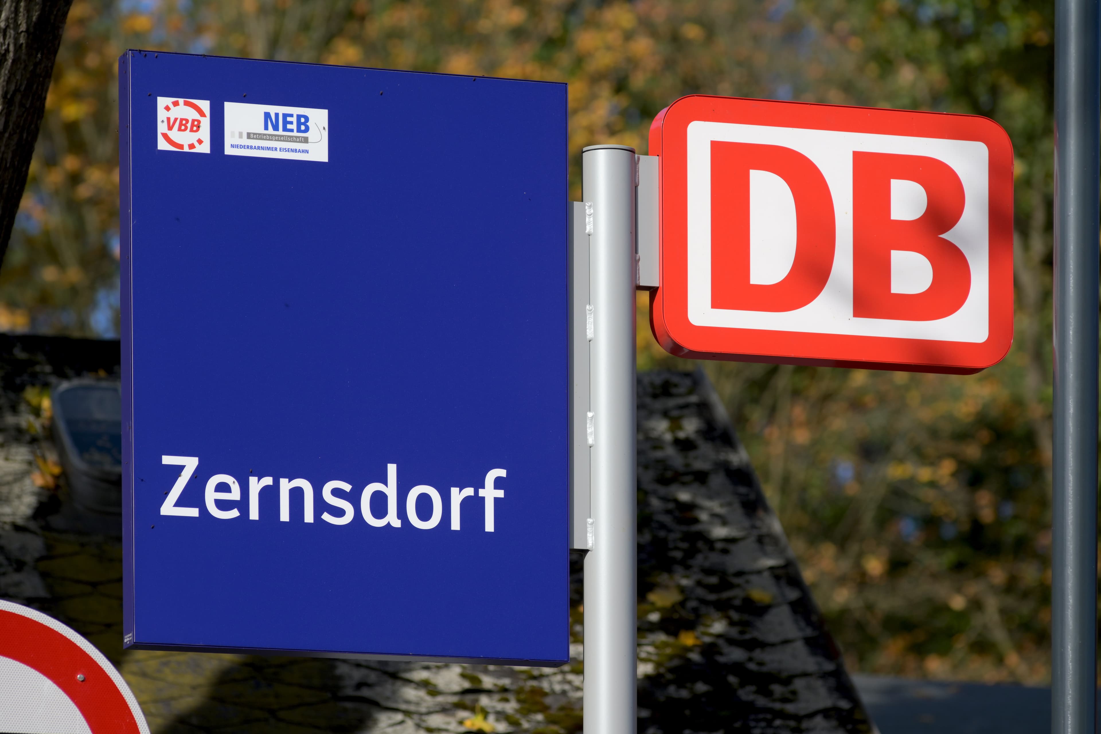 Ein blaues Ortsschild neben einem großen, roten DB-Logo. 